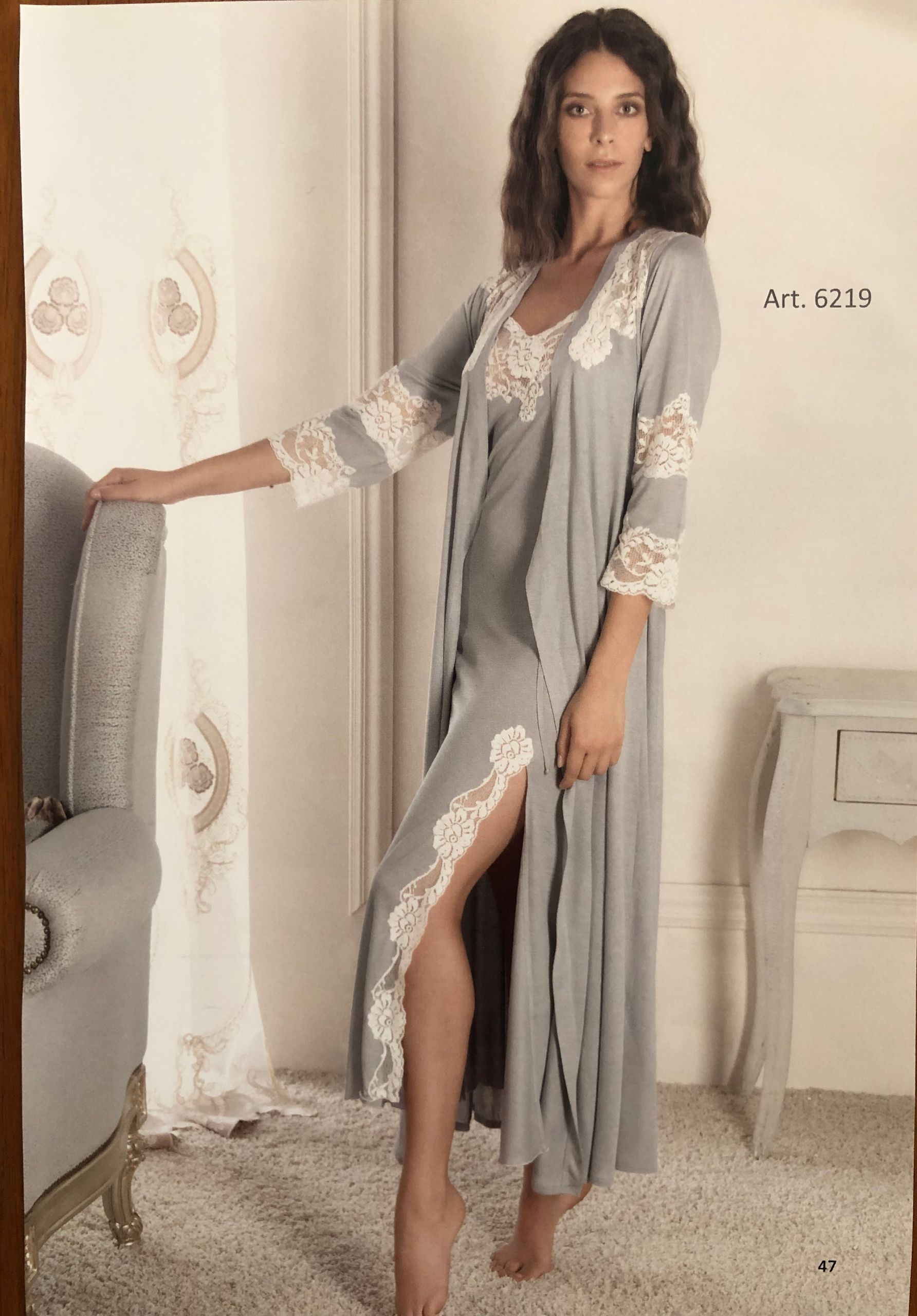 Donna in camicia da notte grigia e vestaglia con bordi in pizzo, in piedi in una stanza.