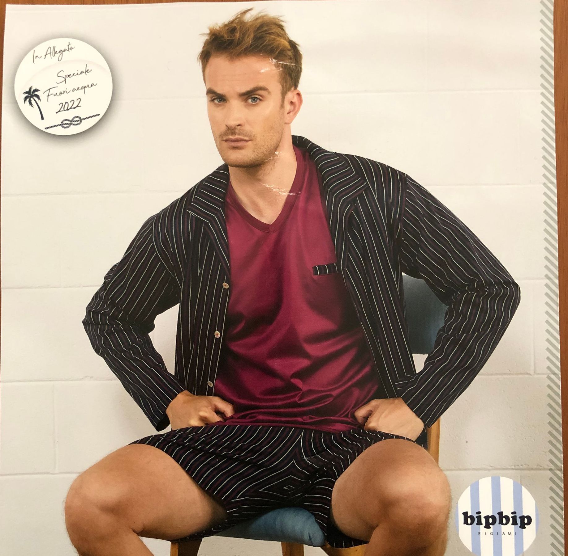 Uomo seduto con giacca a righe, pantaloncini e camicia bordeaux.