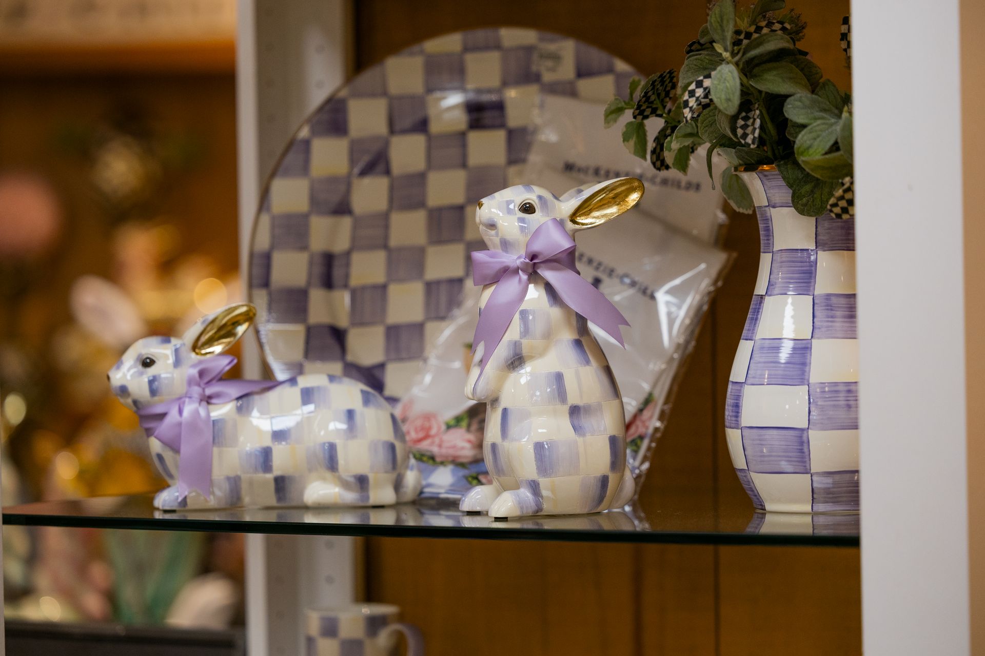 Purple-and-white checkered ceramic bunny figurines on a shelf with a plate and plant in the background