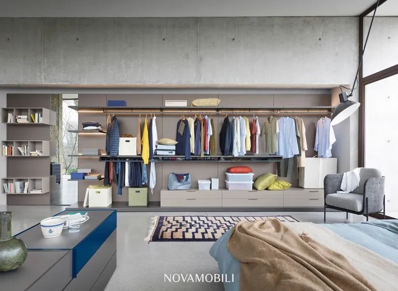 Cabina armadio moderna con appendiabiti, ripiani, cassetti e una sedia grigia.