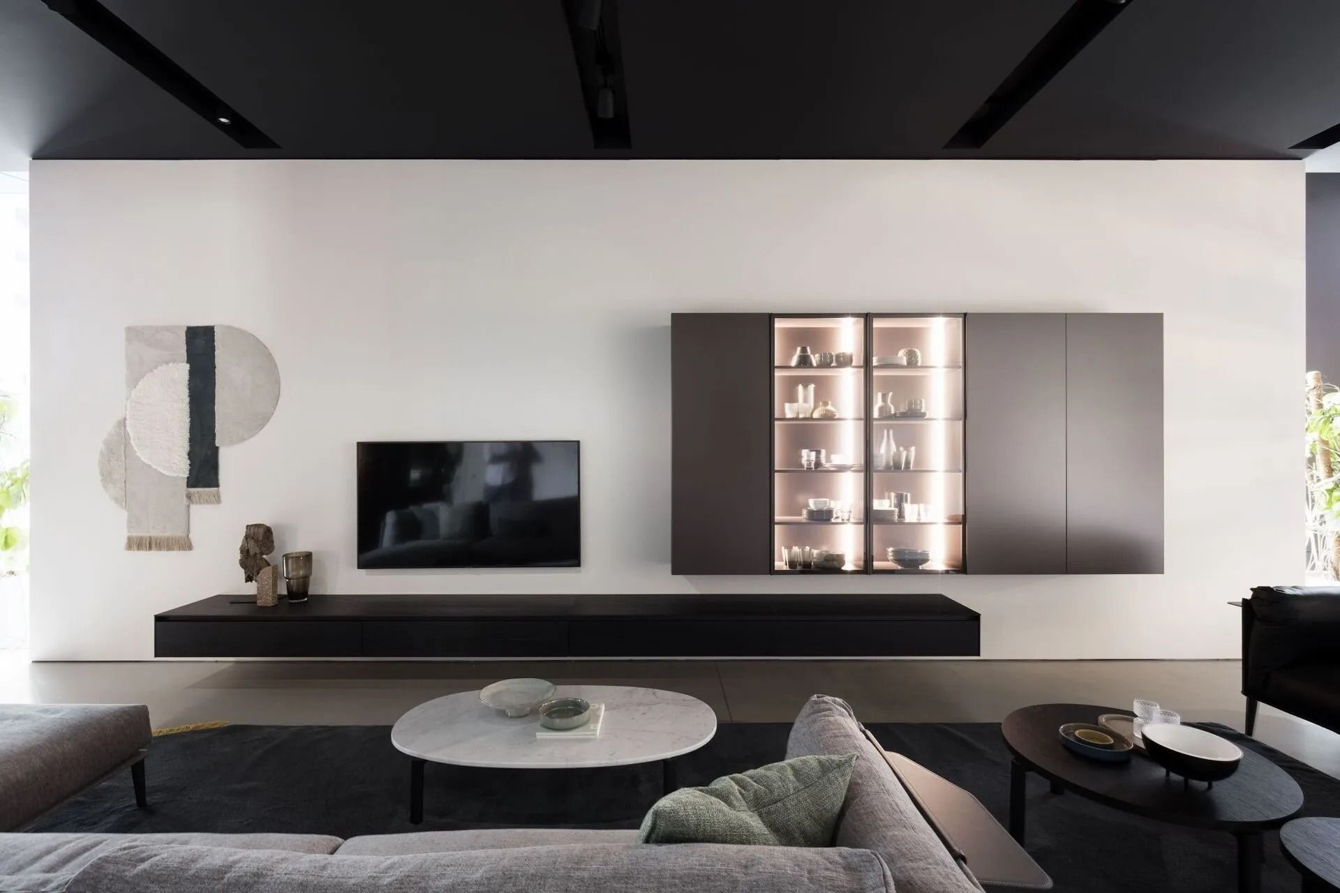 Soggiorno moderno e minimalista con TV a parete, mensole integrate e arredamento neutro nei toni del nero, bianco e grigio.