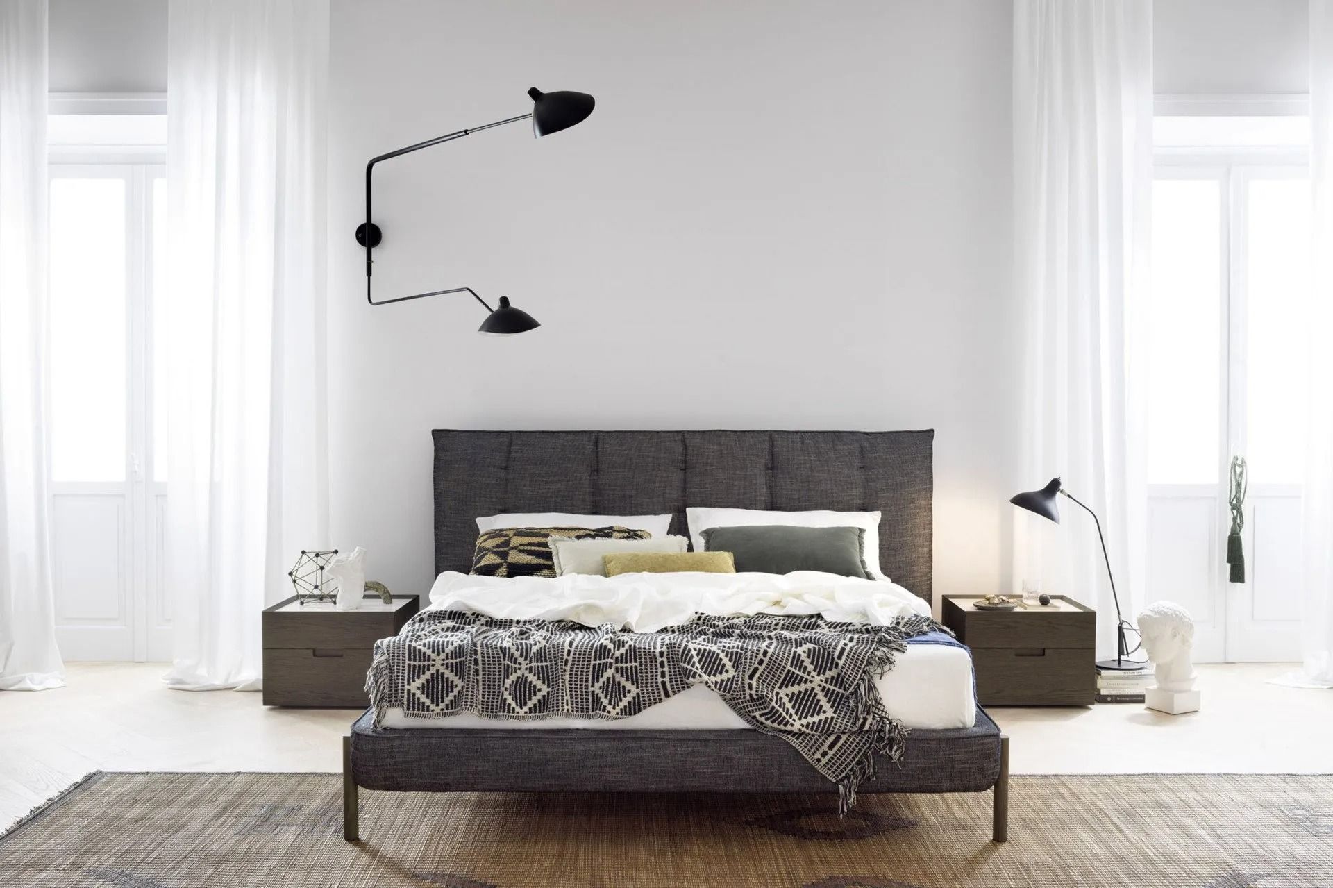 Luminosa camera da letto moderna con letto imbottito scuro, lenzuola bianche e lampade a parete.