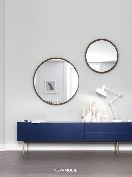 Camera minimalista con credenza blu navy, due specchi rotondi e una lampada da scrivania bianca su una parete grigia.