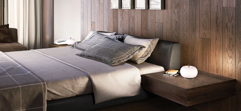 Camera da letto moderna con biancheria da letto grigia, parete rivestita in legno e comodino con lampada.