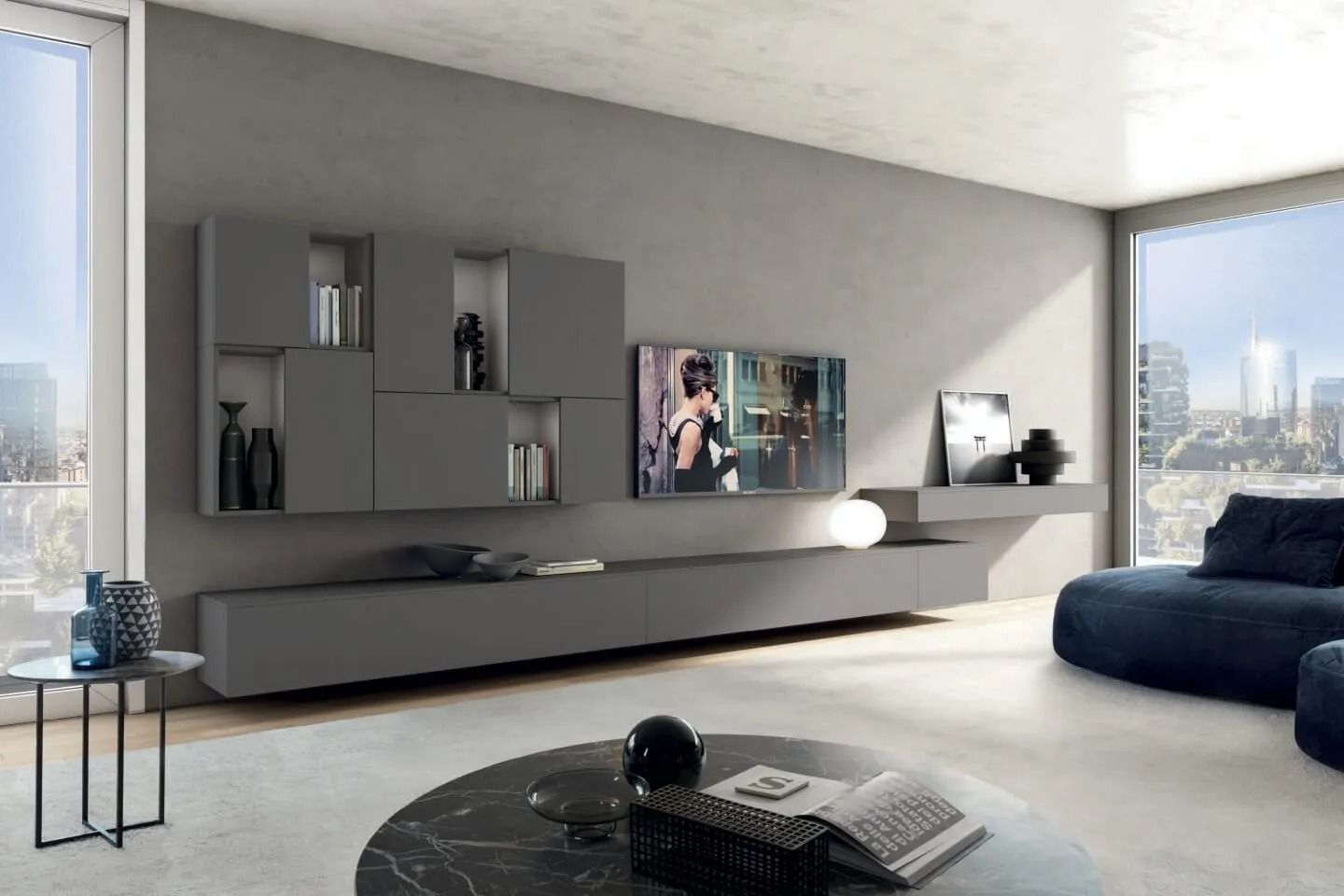 Soggiorno moderno con mensole a muro grigie, TV, divano scuro e vista sulla città attraverso ampie finestre.