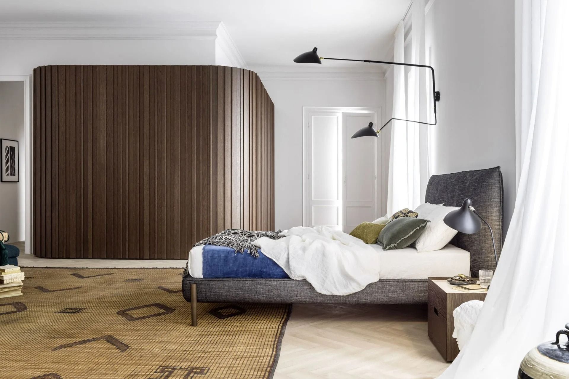 Camera da letto minimalista con letto, parete rivestita in legno e tende bianche luminose.