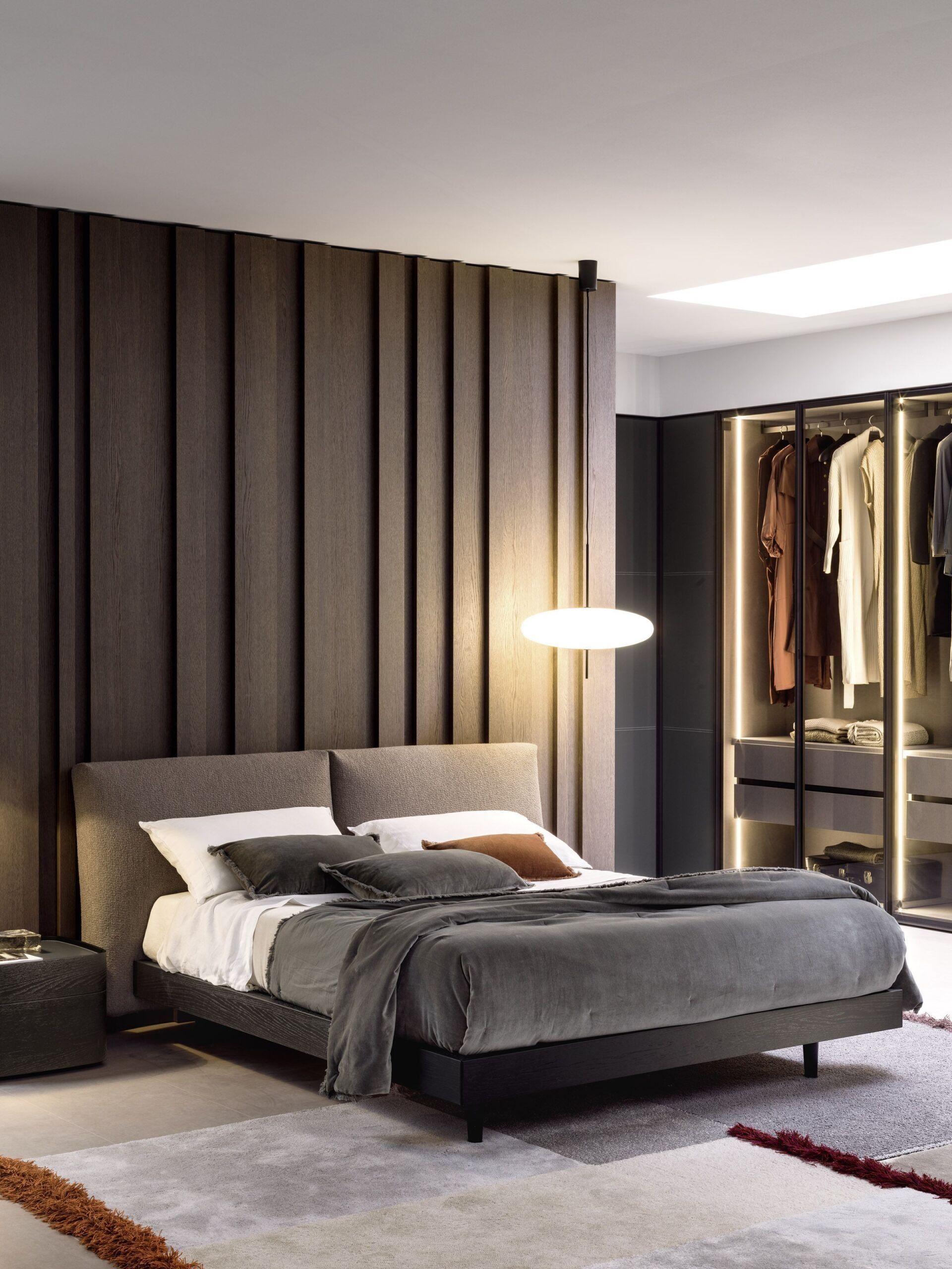 Camera da letto moderna con letto scuro, parete decorativa in legno a righe, lampada a sospensione e armadio a giorno.