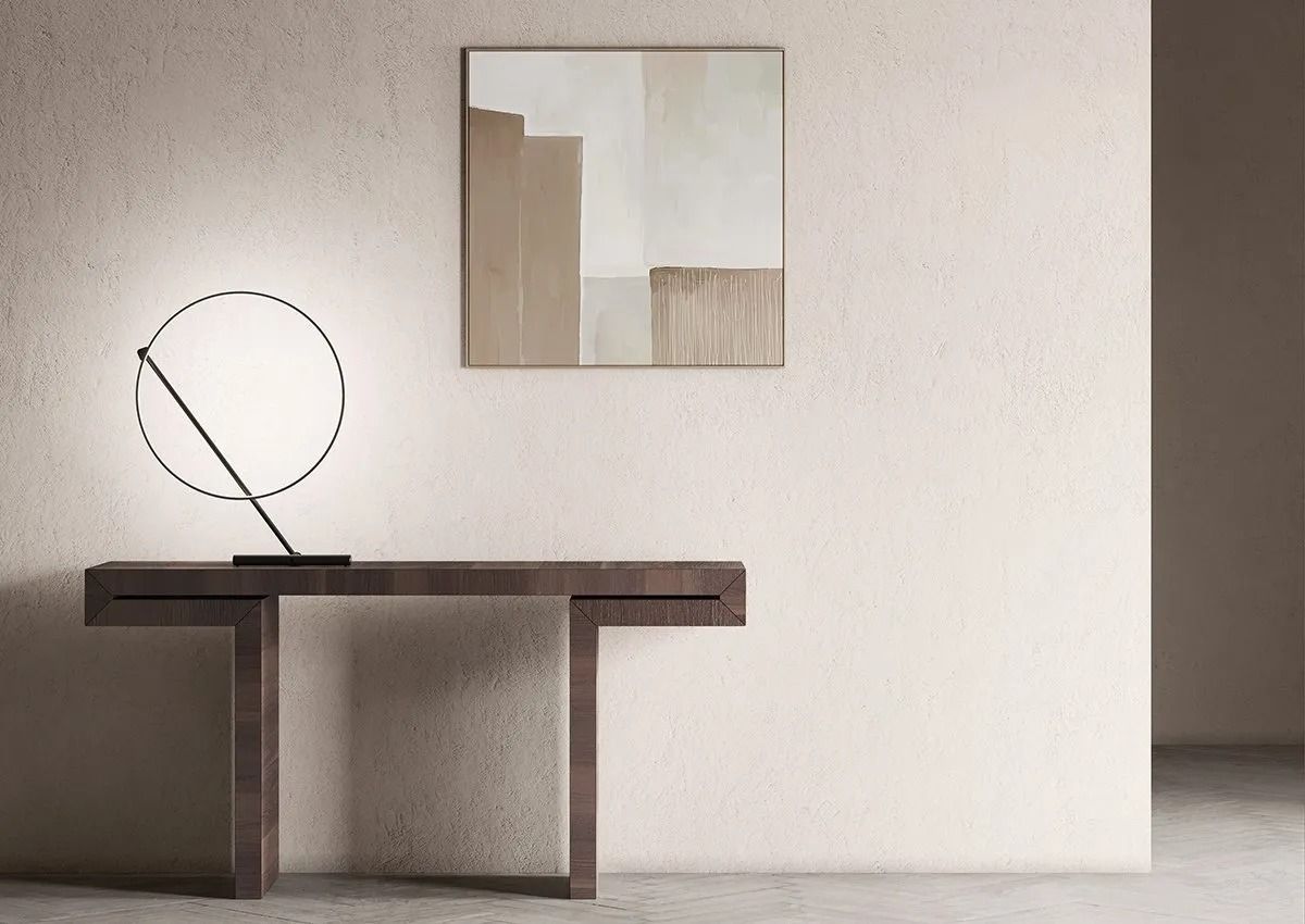 Stanza minimalista con consolle scura, lampada circolare e quadro astratto su una parete bianca.