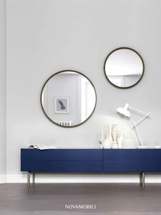 Camera moderna grigia con due specchi rotondi sopra una consolle blu scuro e una lampada da scrivania bianca.