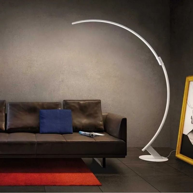 Soggiorno moderno con divano scuro, tappeto rosso e lampada da terra ad arco bianca accanto a uno specchio