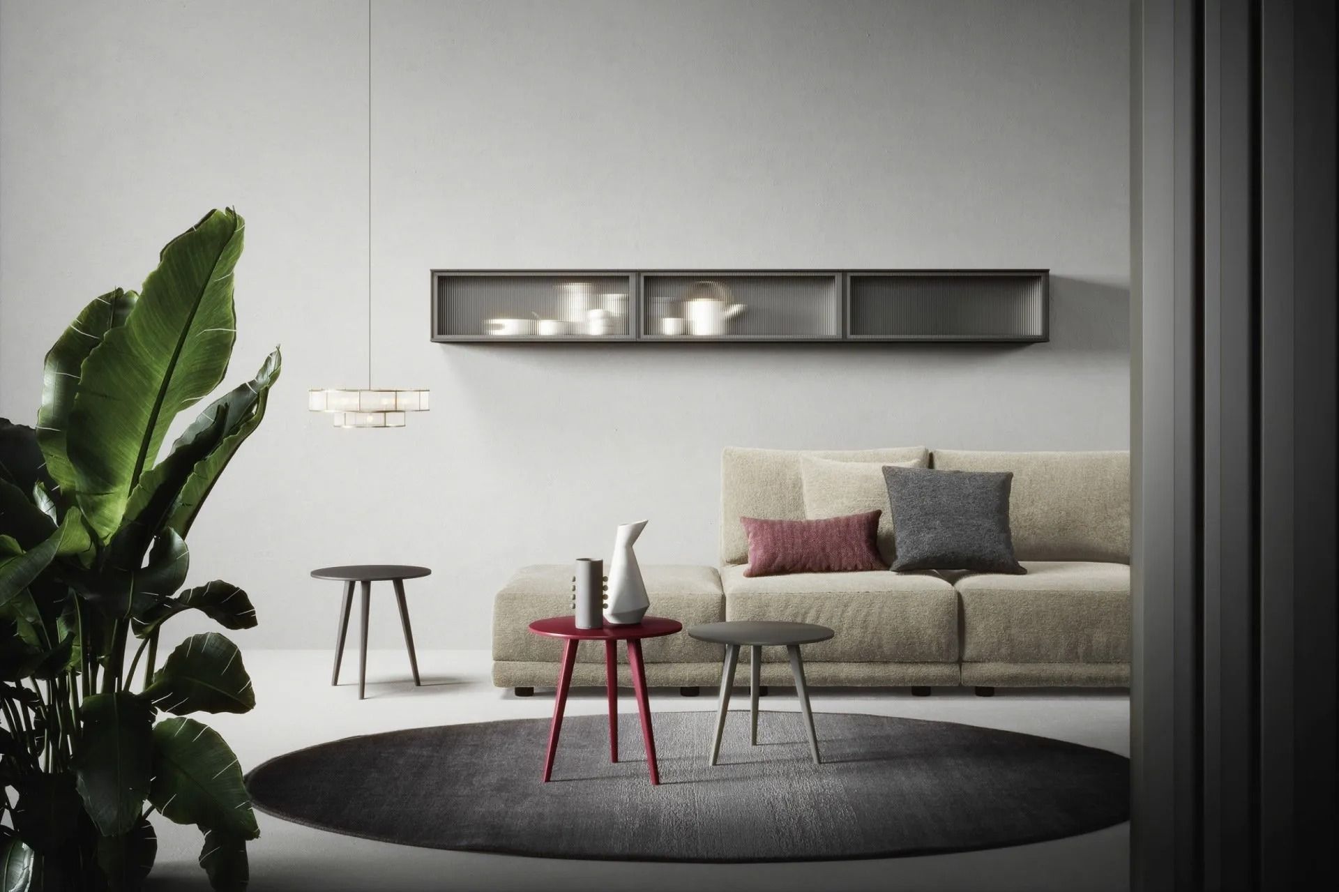 Soggiorno minimalista con divano beige, tappeto rotondo, tavolini e grande pianta accanto a una parete bianca.