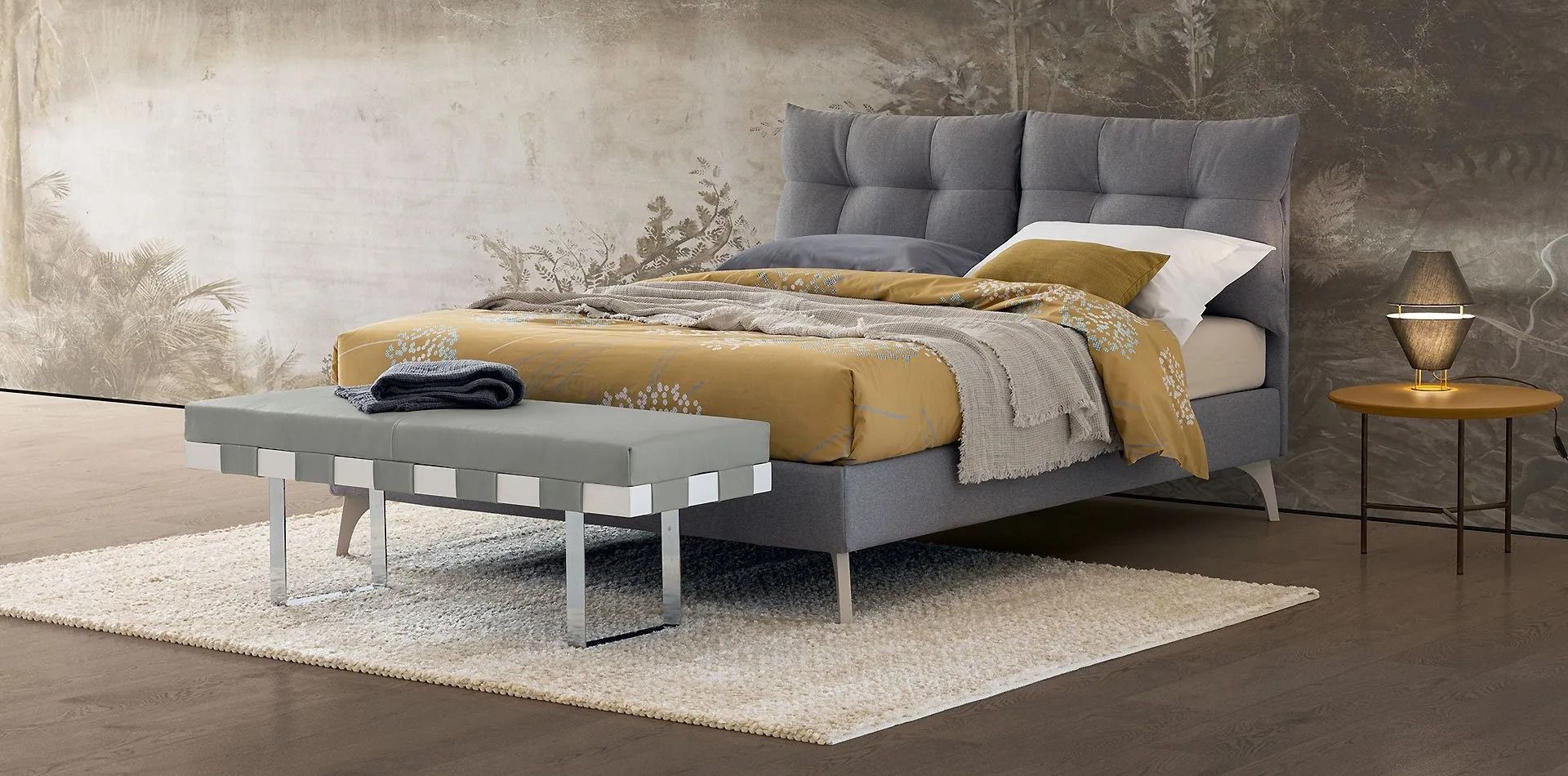 Camera da letto moderna con letto grigio, lenzuola color senape, lampada da comodino e tappeto.