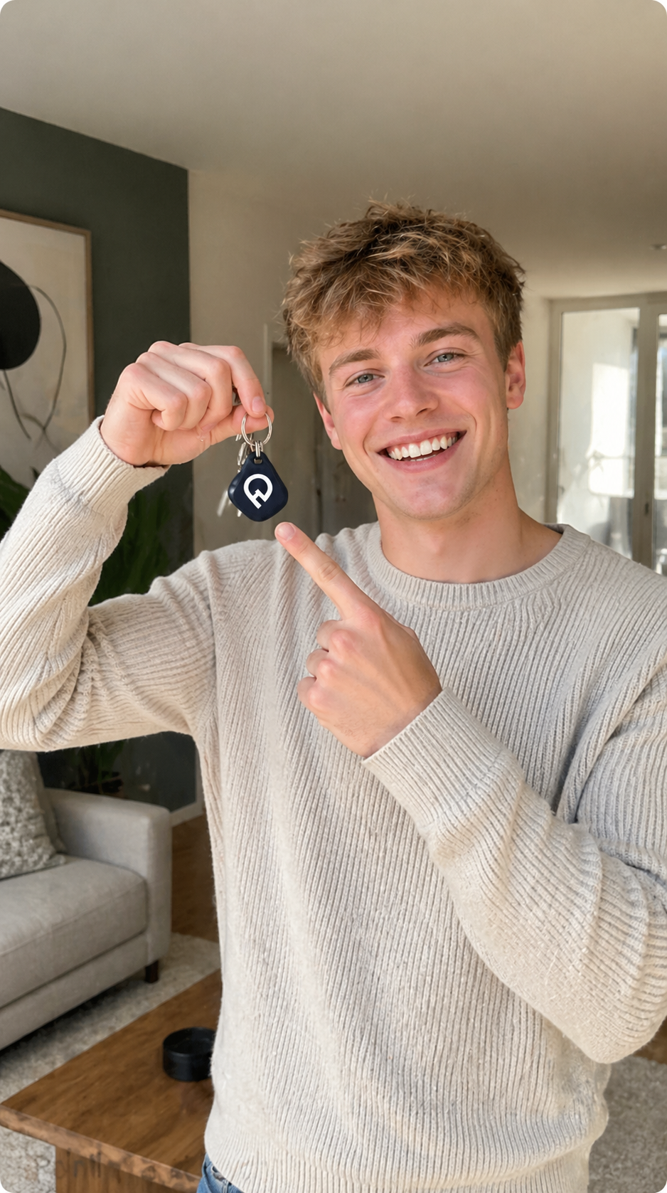 Smiling person in a cream sweater holding up a small black item indoors, pointing at it.