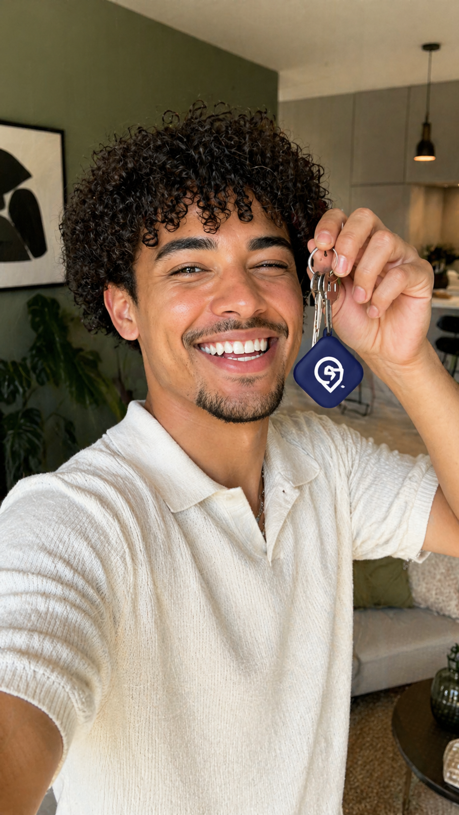 Smiling person holding up a small blue key tag indoors, wearing a white shirt.