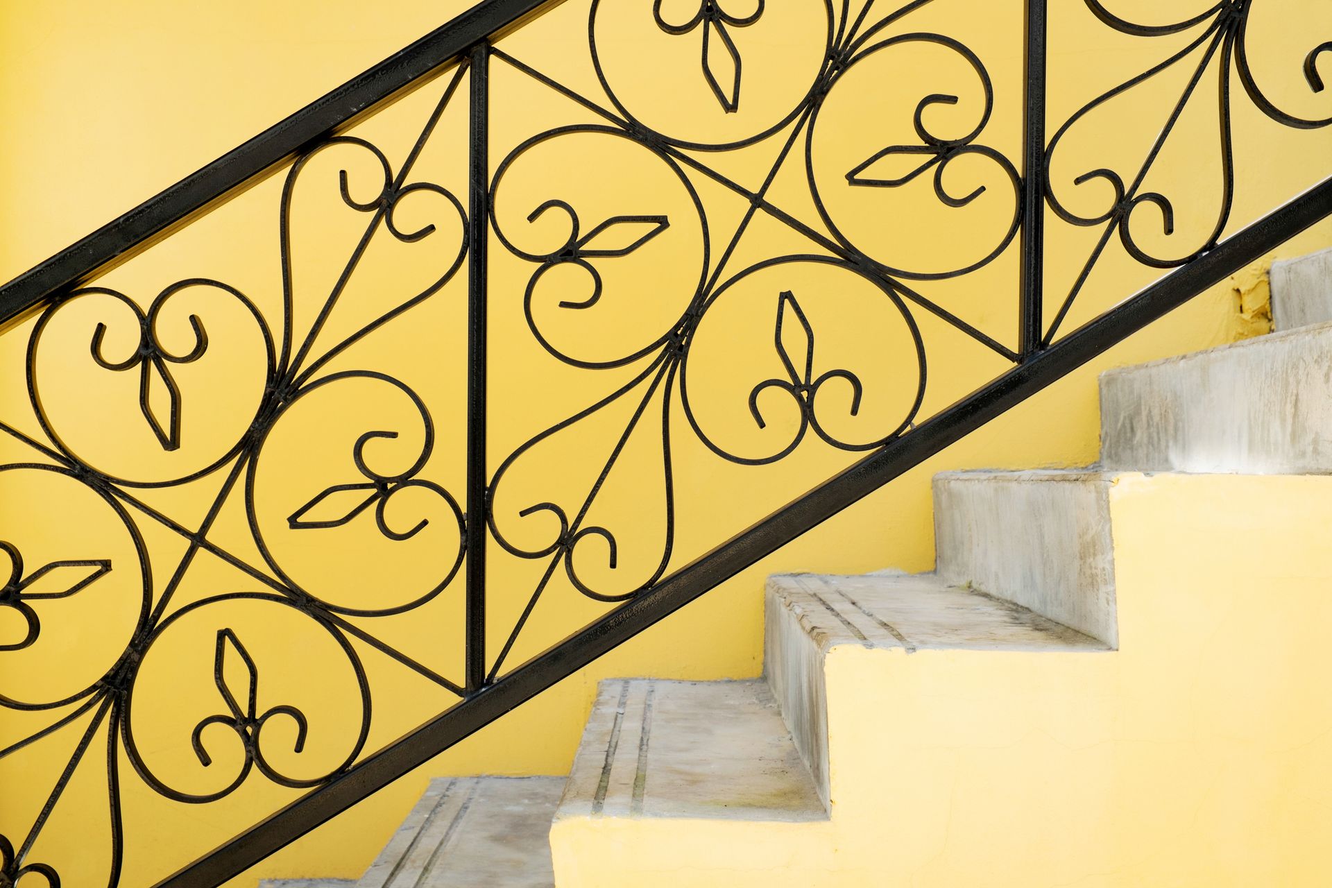 Ringhiera in ferro battuto nero con spirali decorative e scale contro una parete gialla.