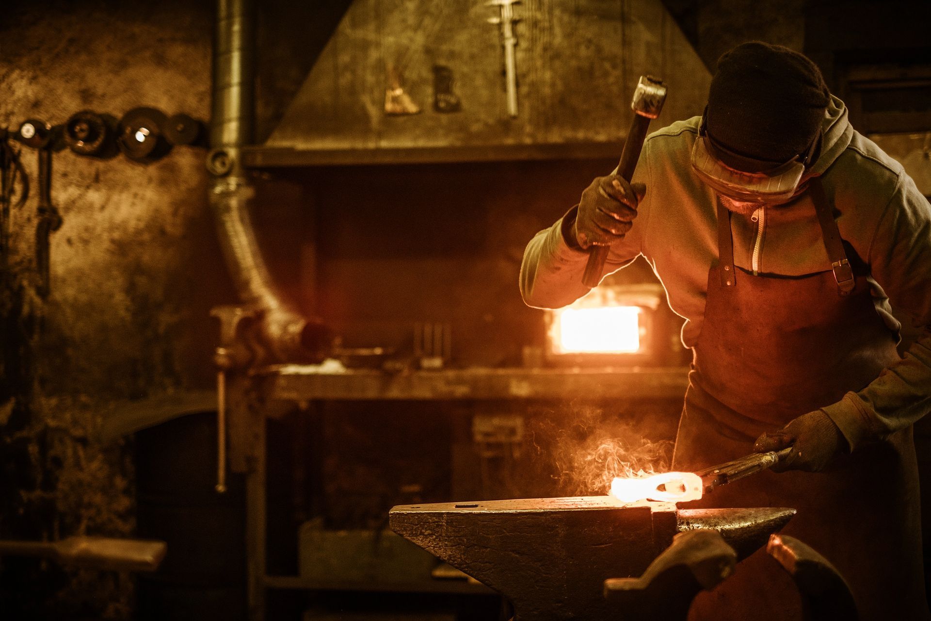 Un fabbro martella il metallo incandescente su un'incudine in un'officina.
