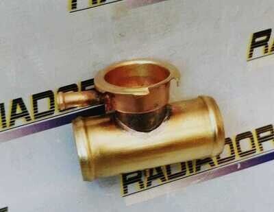 Conector de tubería de metal color oro con válvula lateral sobre fondo blanco con logotipo.