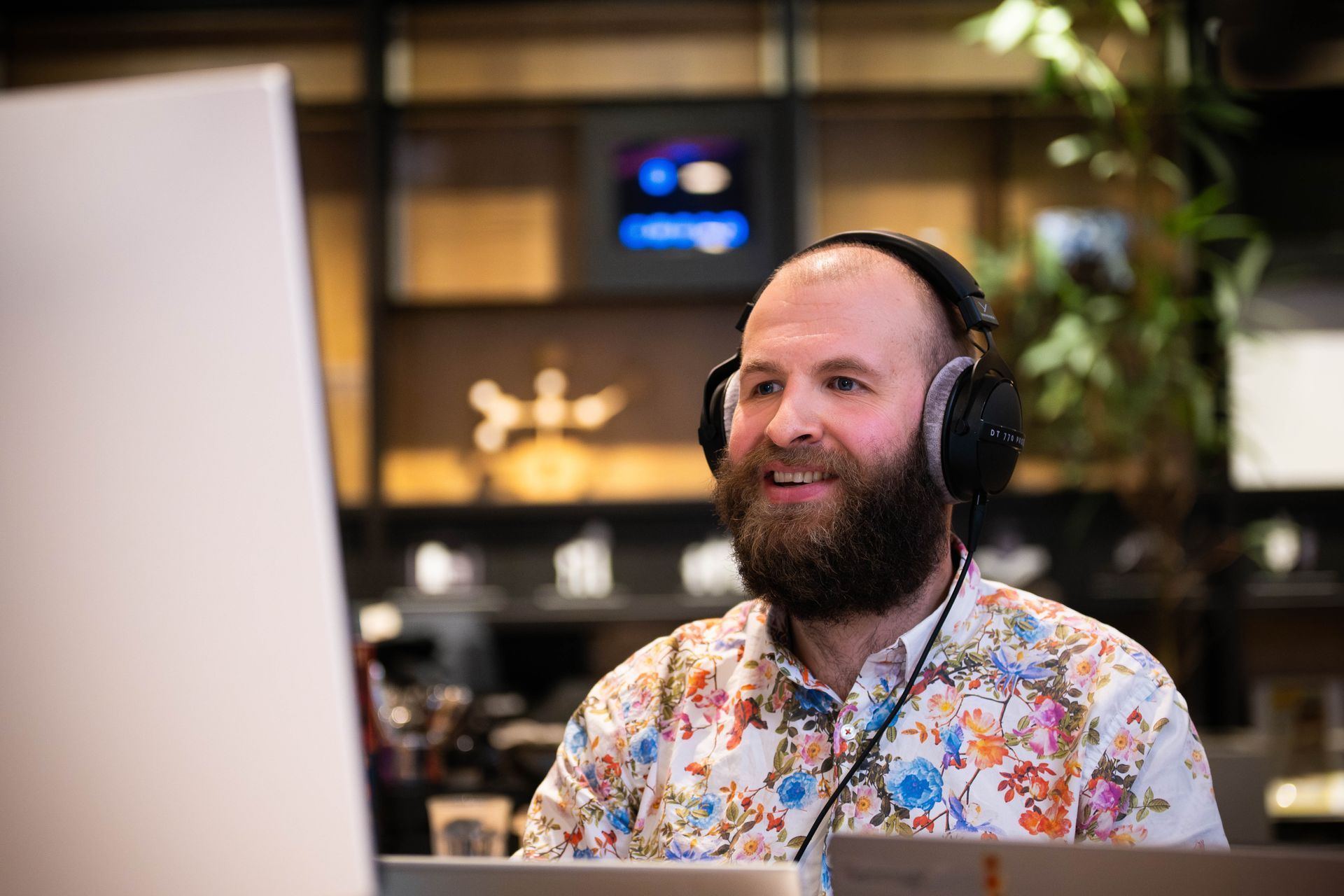 Een bebaarde persoon met een koptelefoon op kijkt naar een computerscherm in een koffiehuis.