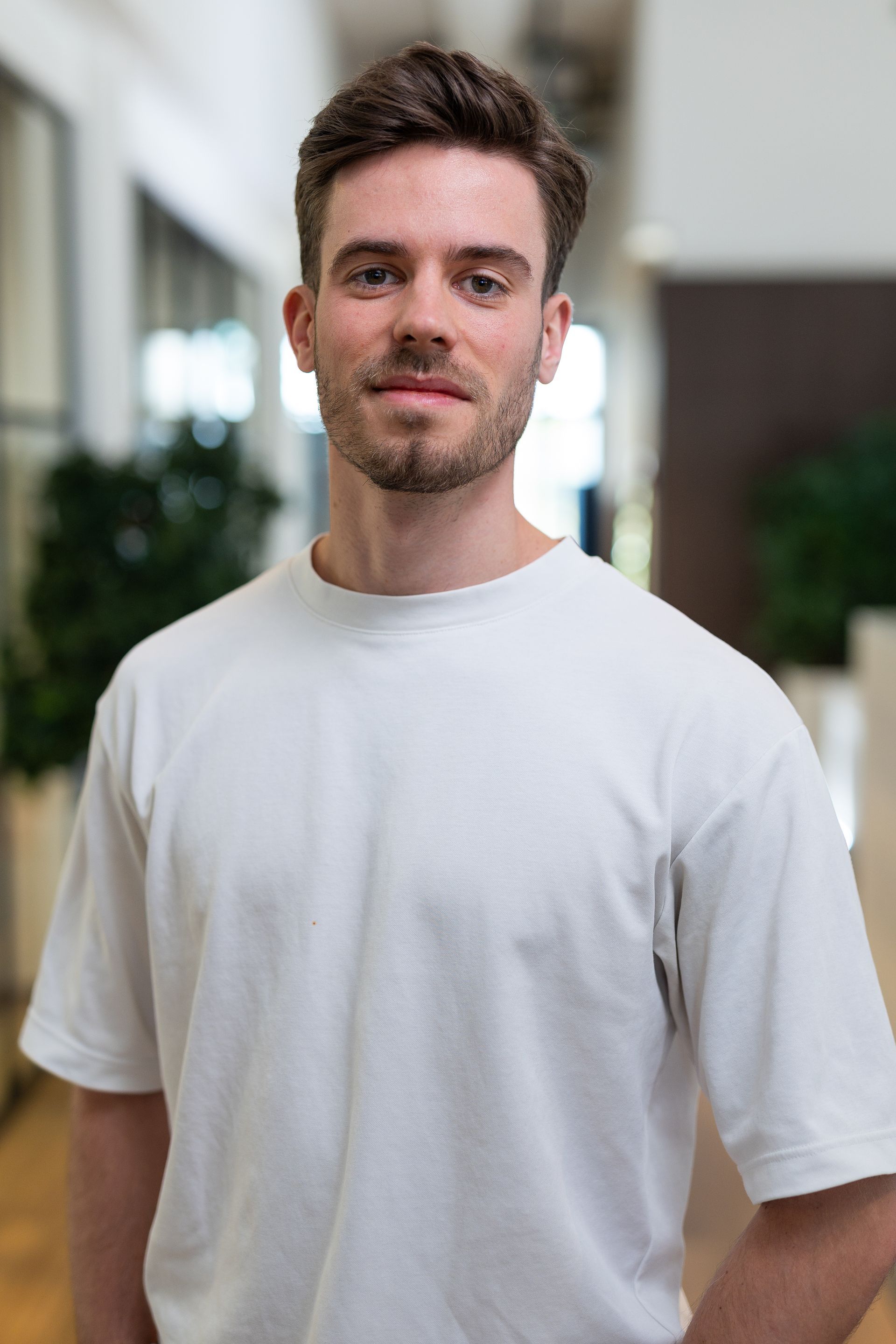 Een man in een wit shirt staat binnen en glimlacht lichtjes.