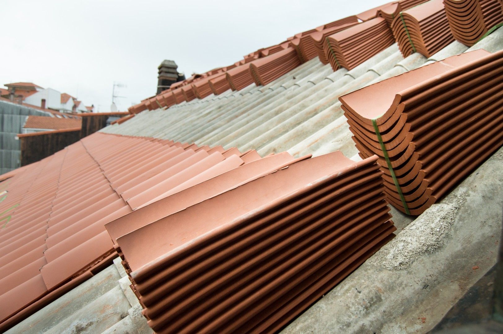 Primo piano di tegole in terracotta e pannelli ondulati impilati su un tetto inclinato in costruzione.