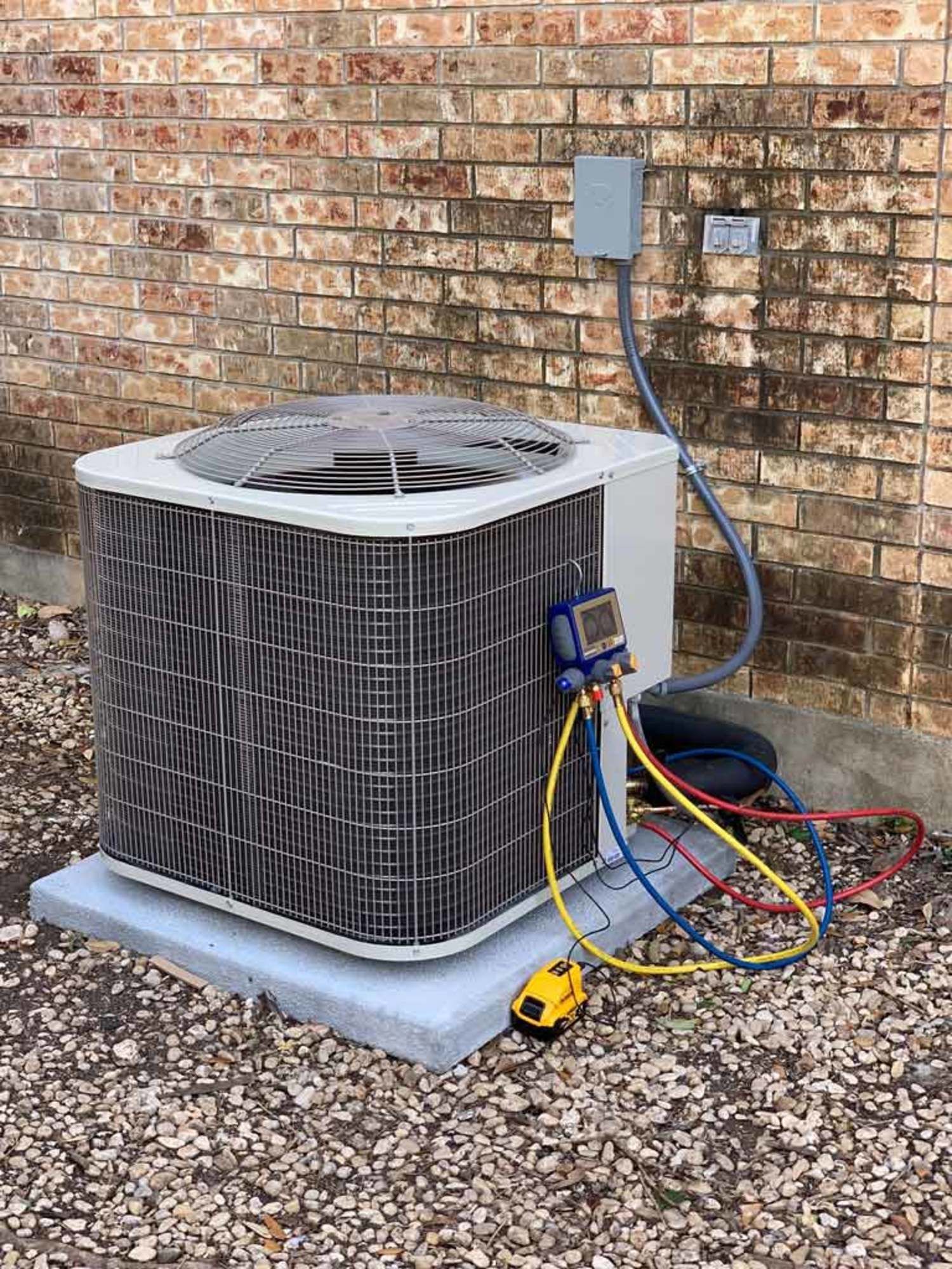 an air conditioner is being serviced in front of a brick wall .