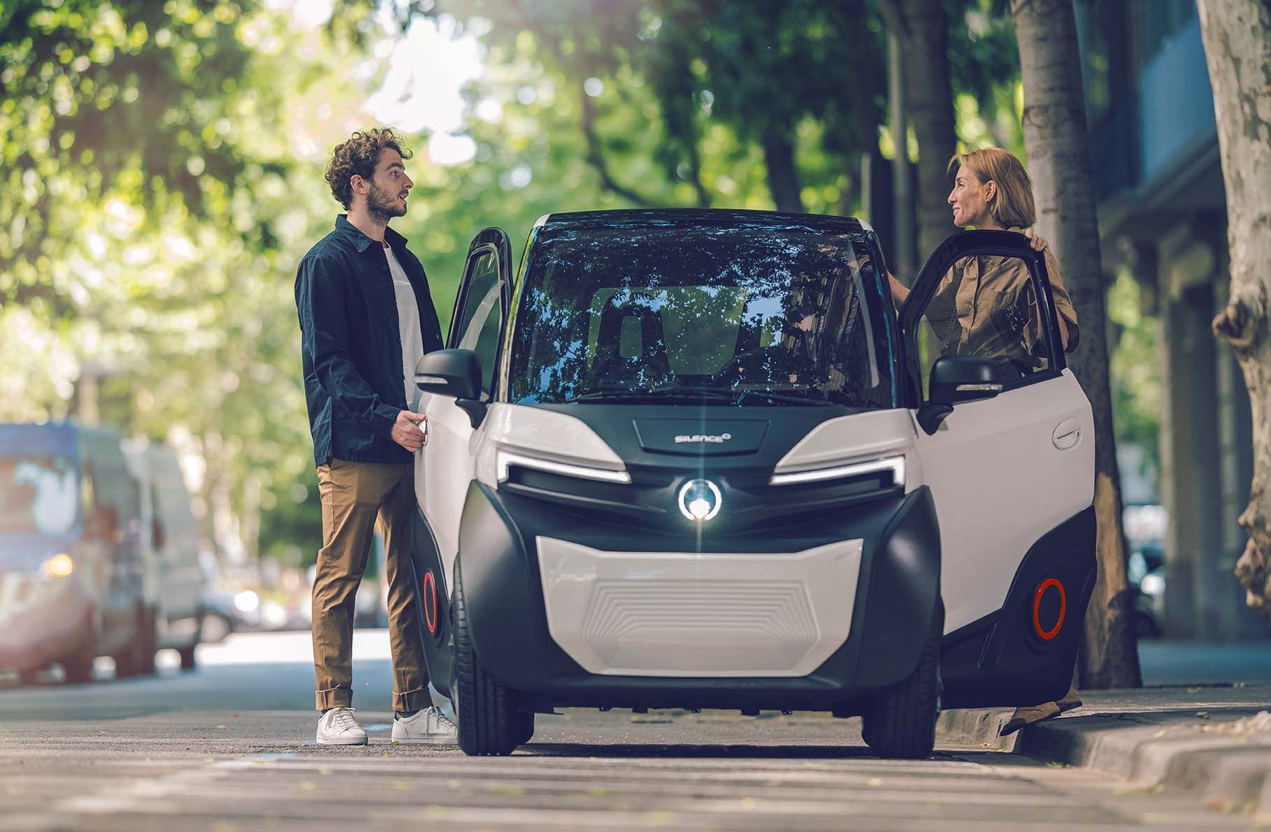Un uomo e una donna sono in piedi accanto a una piccola auto elettrica.