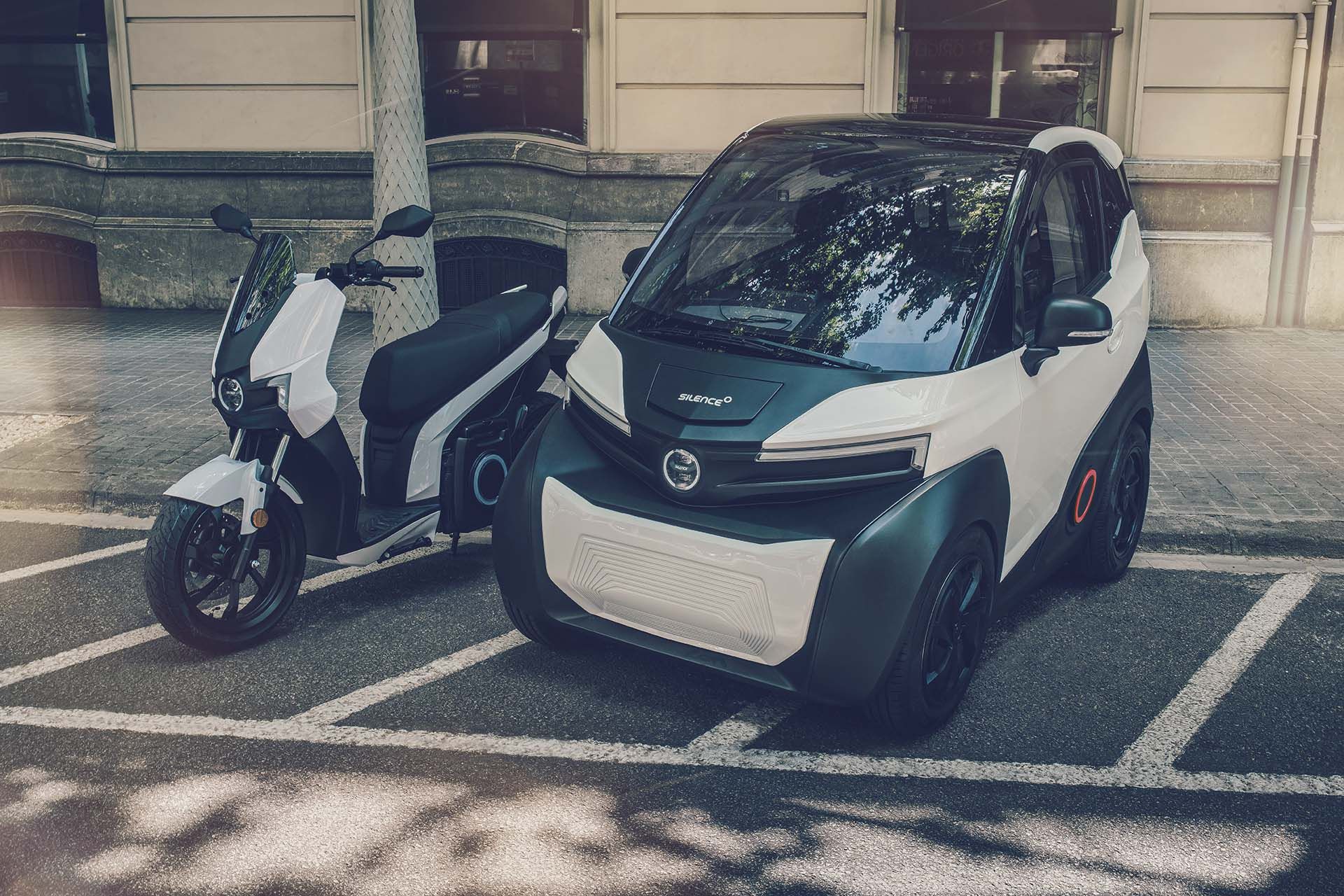 Un'auto e uno scooter sono parcheggiati uno accanto all'altro in un parcheggio.