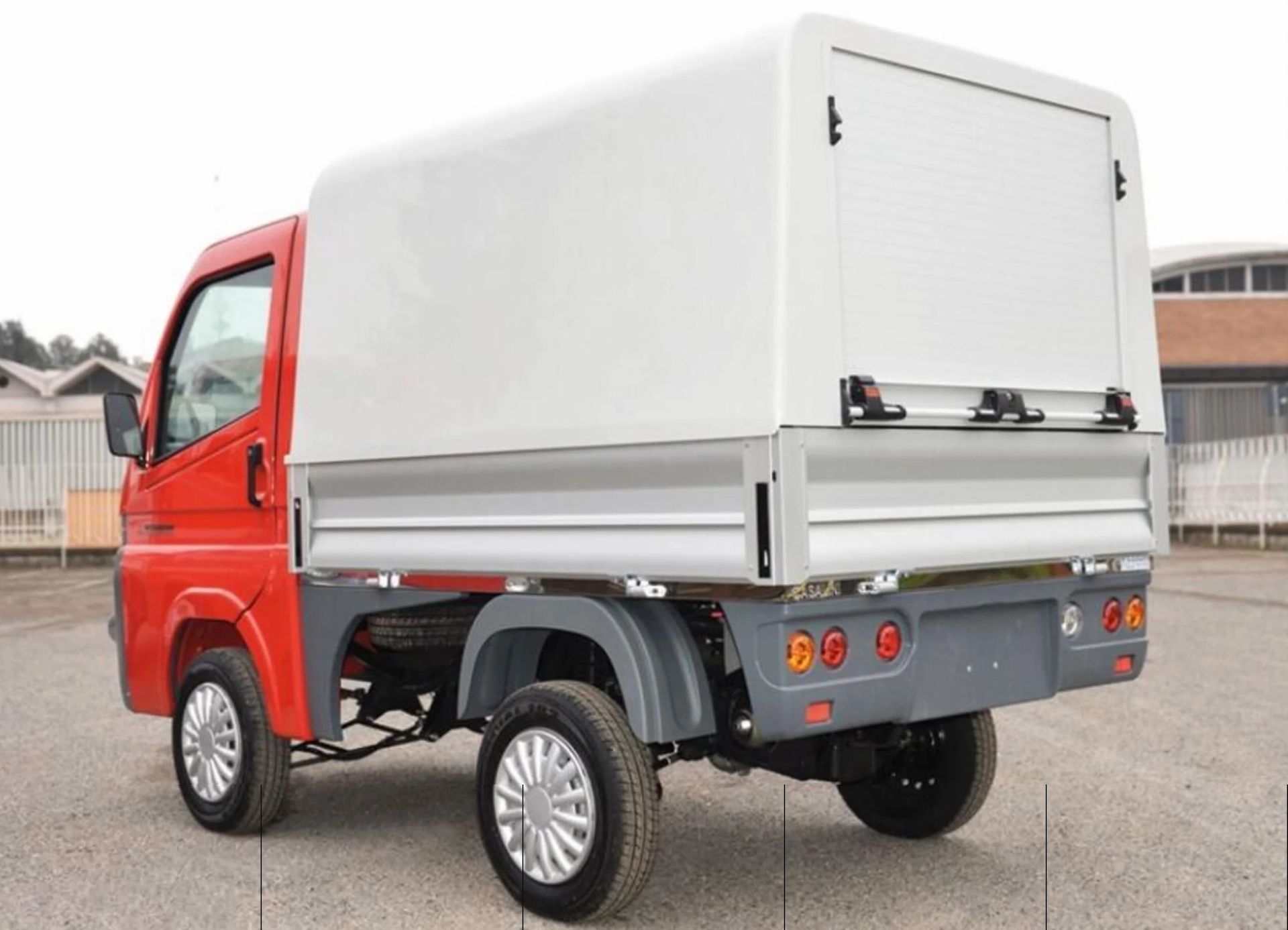 Un camion rosso con una tettoia bianca è parcheggiato in un parcheggio.