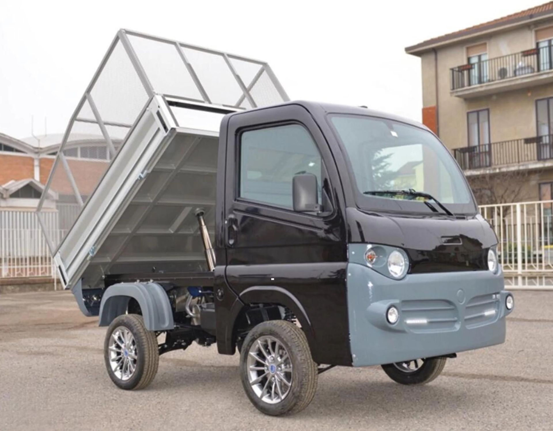 Un camion con cassone ribaltabile nero e grigio è parcheggiato davanti a un edificio.