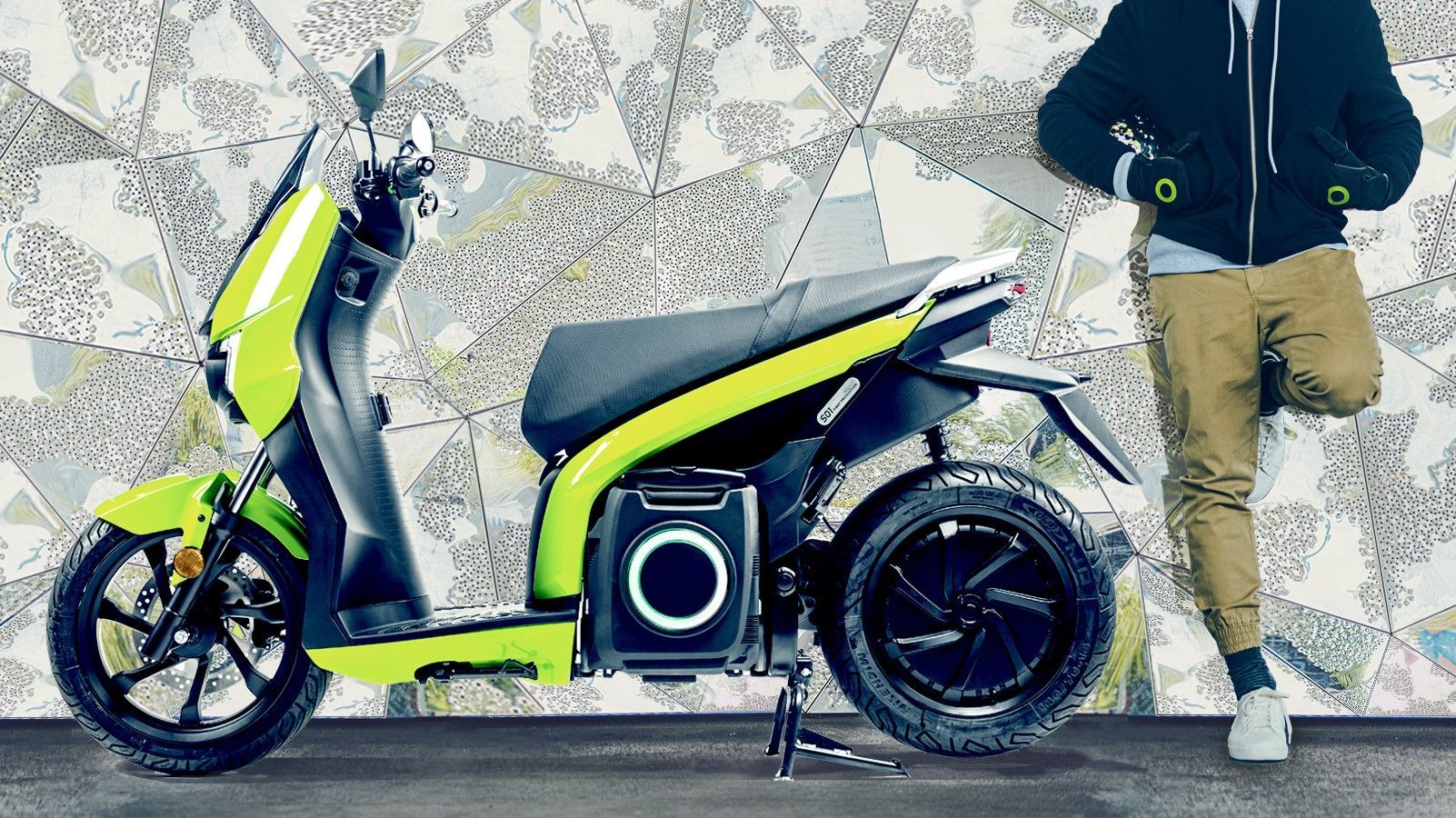 Un uomo è appoggiato a un muro accanto a uno scooter.