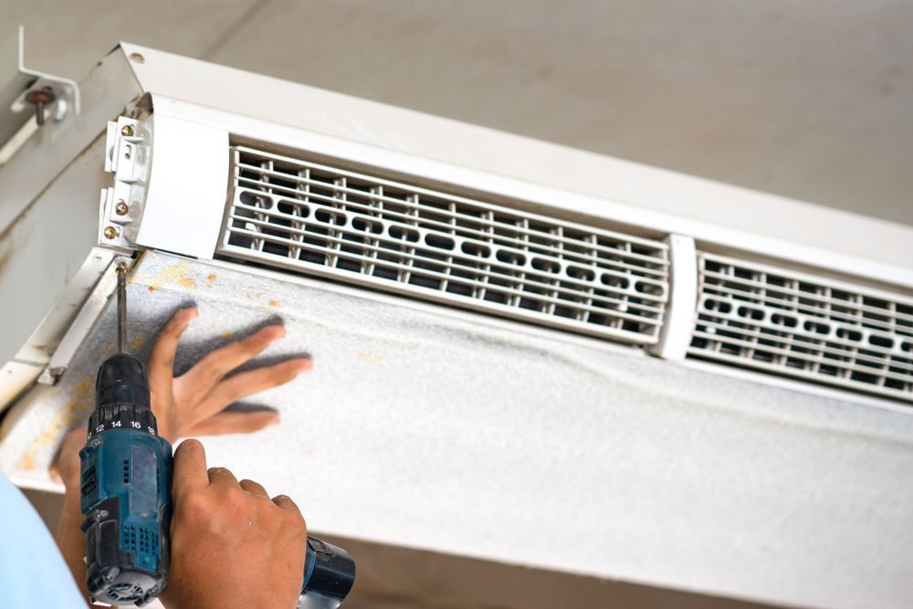 A Man Is Using a Drill to Fix an Air Conditioner — Revive Air Conditioning in Oran Park, NSW