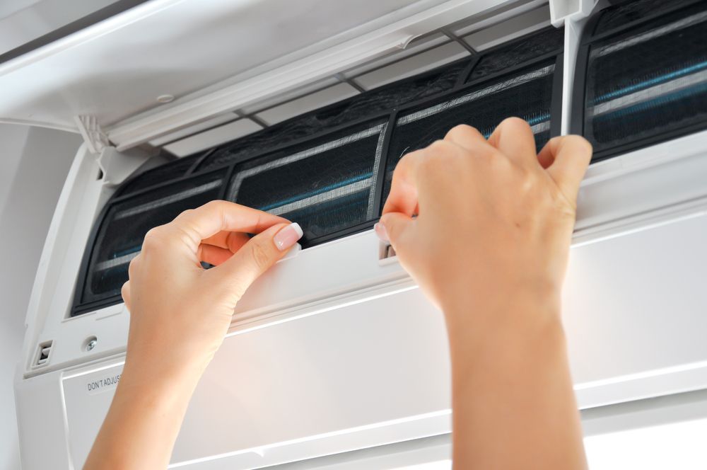 A Person is Cleaning an Air Conditioner With a Screwdriver — Revive Air Conditioning in Liverpool, NSW