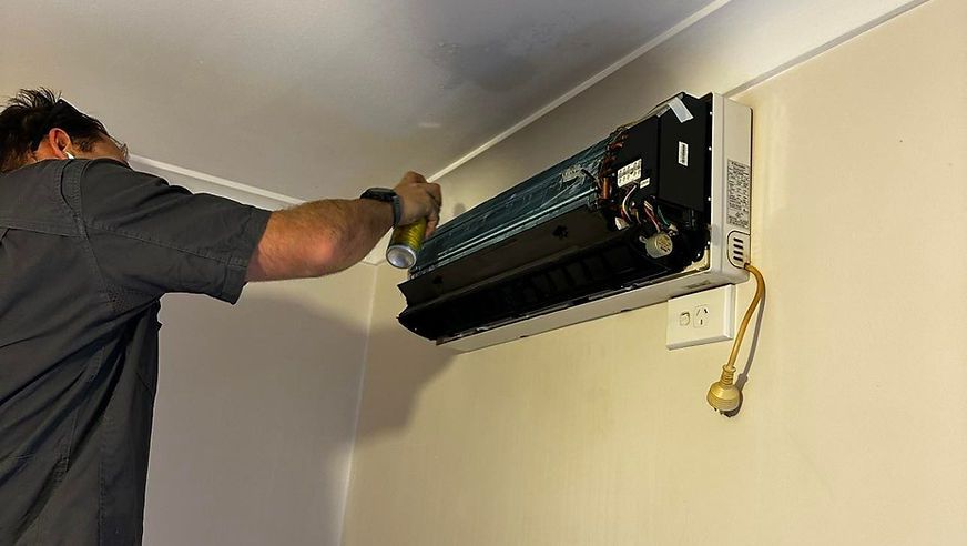 A Man Is Working on An Air Conditioner on A Wall — Revive Air Conditioning in Campbelltown, NSW