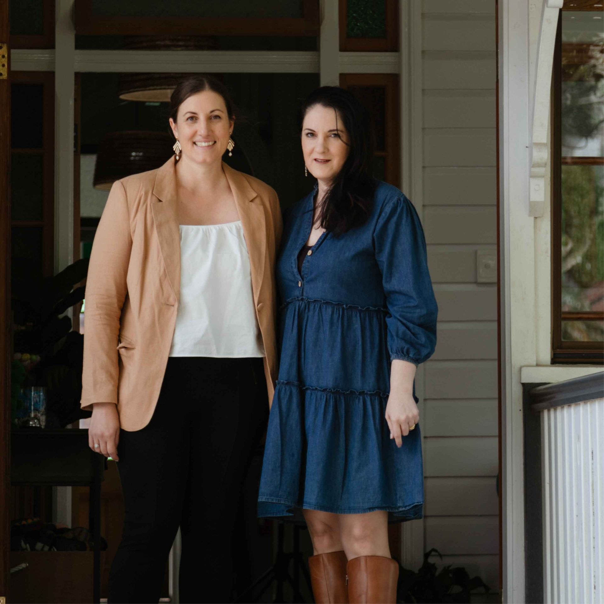 Two women standing on a porch, one in a tan blazer and the other in a blue dress.