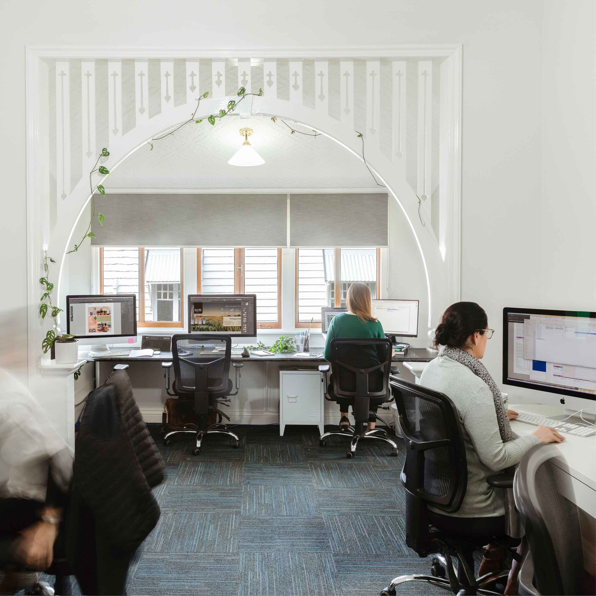 Open office with people working at computers beside white partition walls and windows