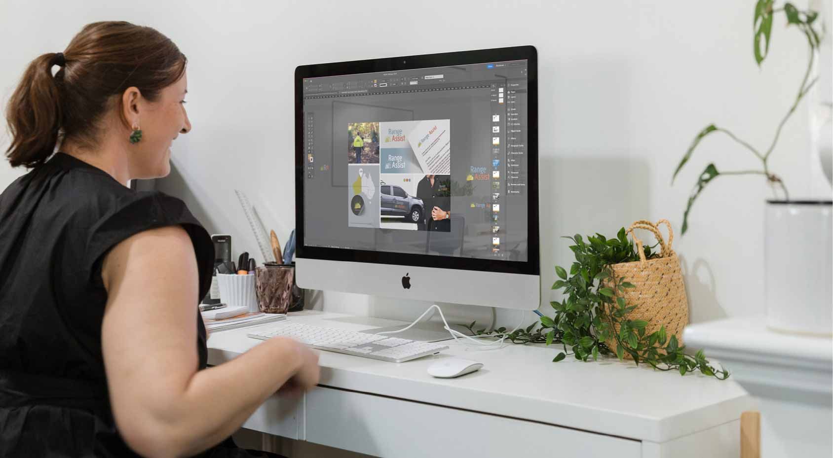 Person working at a desktop computer on a bright white desk with plants nearby