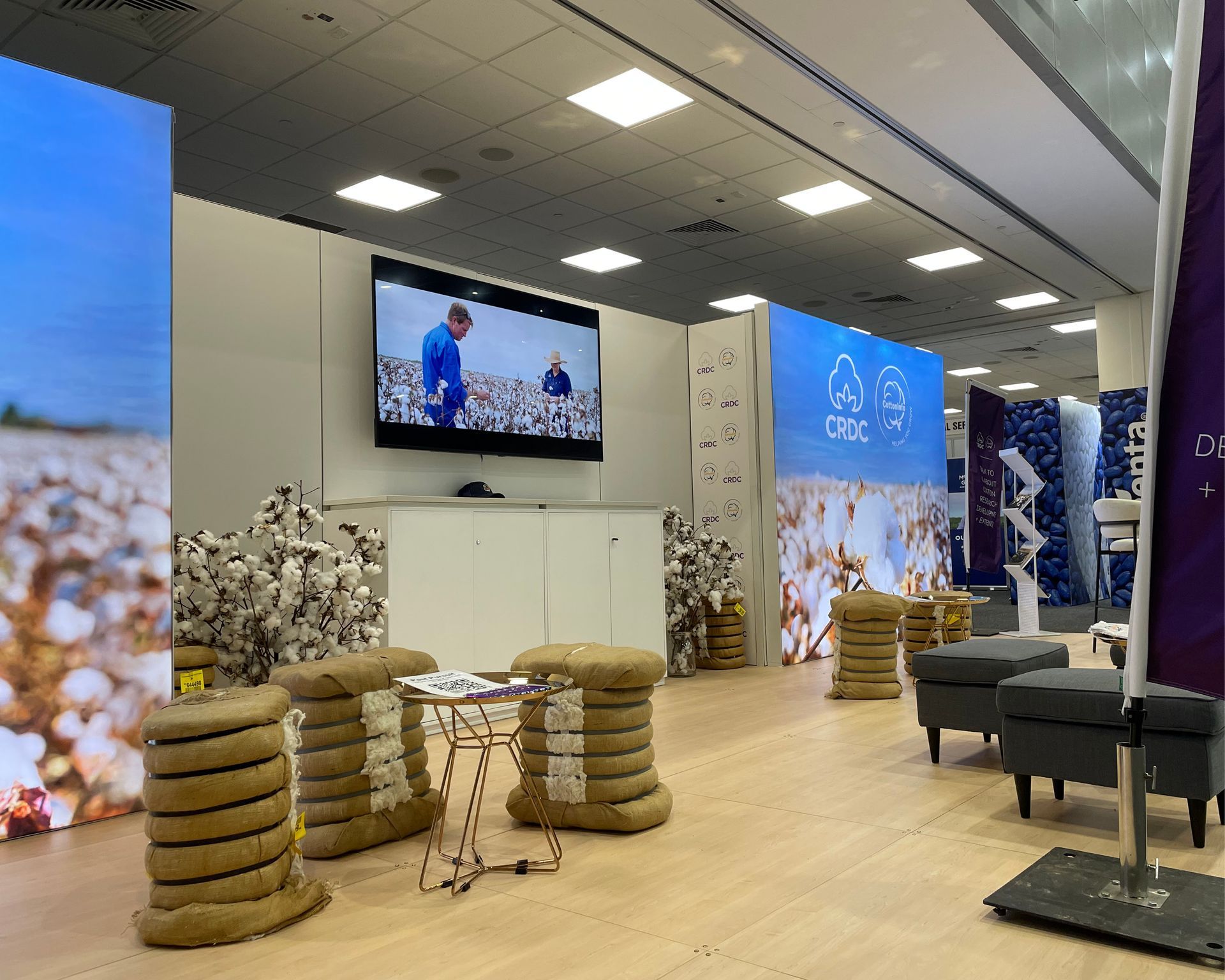 Modern office lounge with stacked wooden stools, white floral decor, wall TVs, and blue accent panels