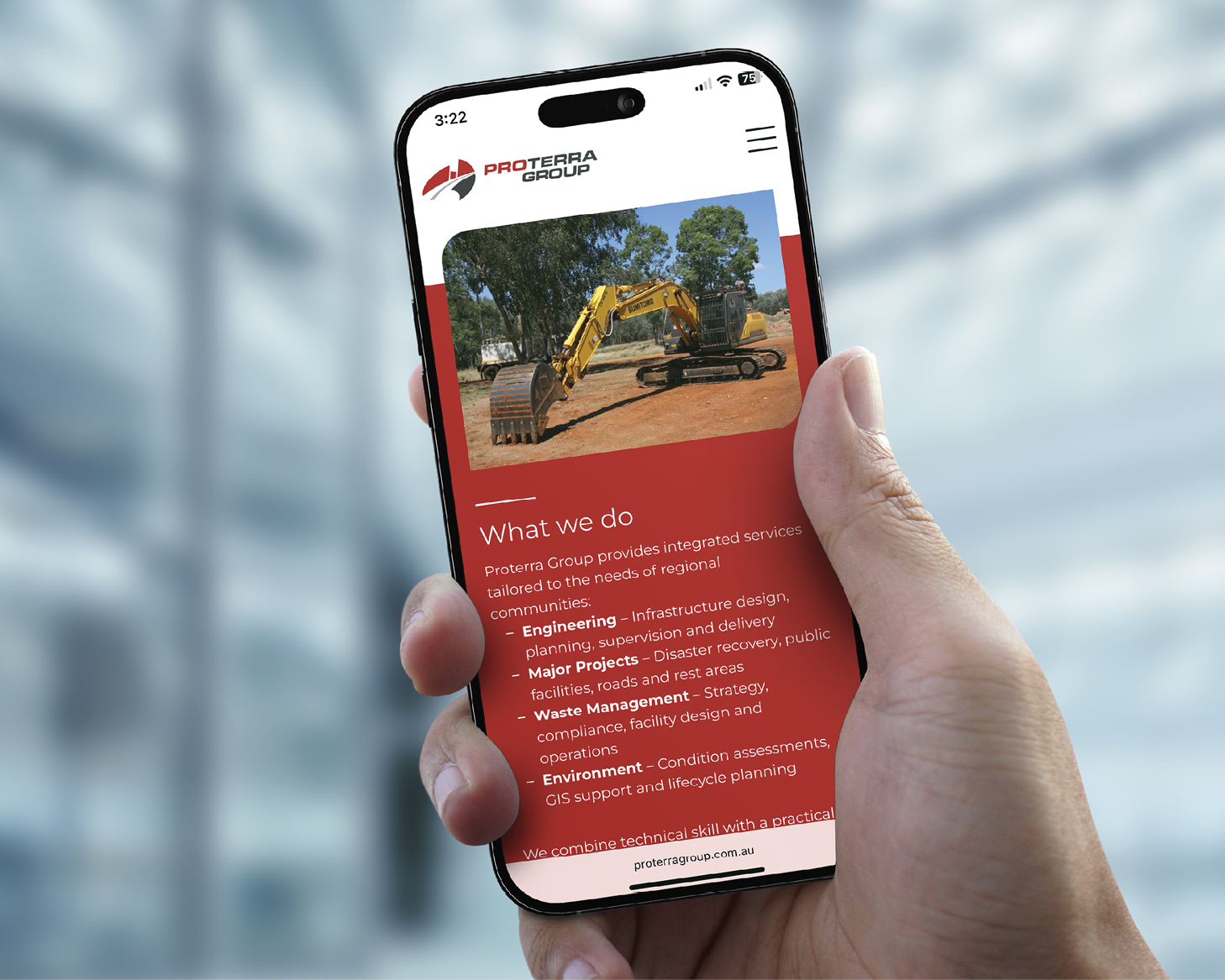 Hand holding a smartphone showing a red webpage with an excavator photo and text over a blurred building background