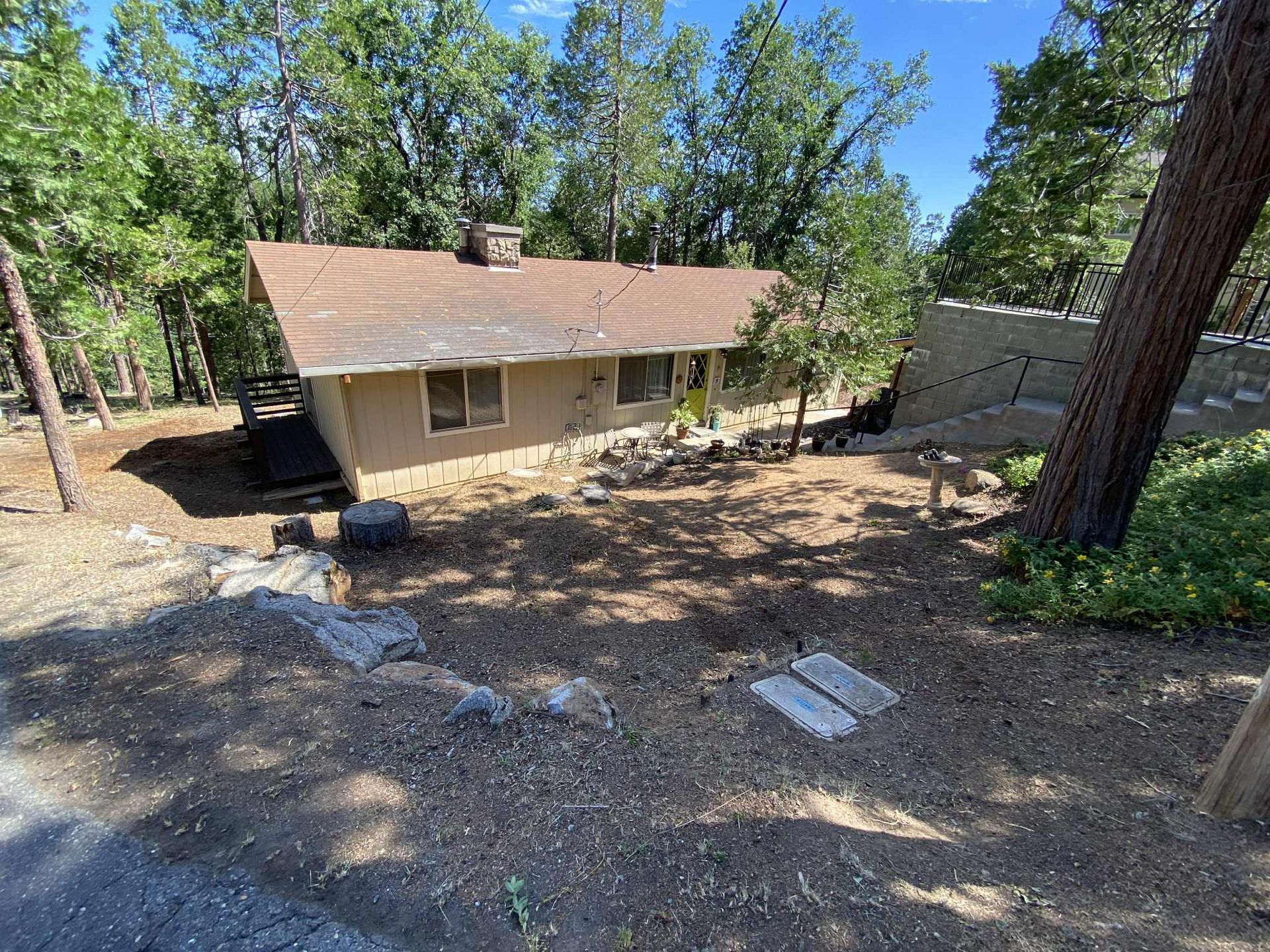 Tan house with a brown roof in a wooded area. The house has steps leading to it.