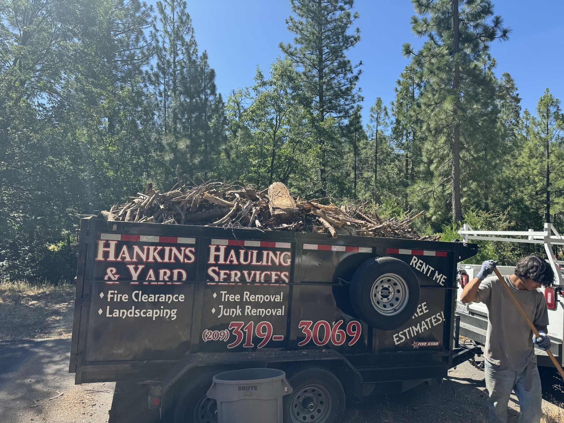 A dumpster overflowing with yard waste; a worker stands near the trailer.