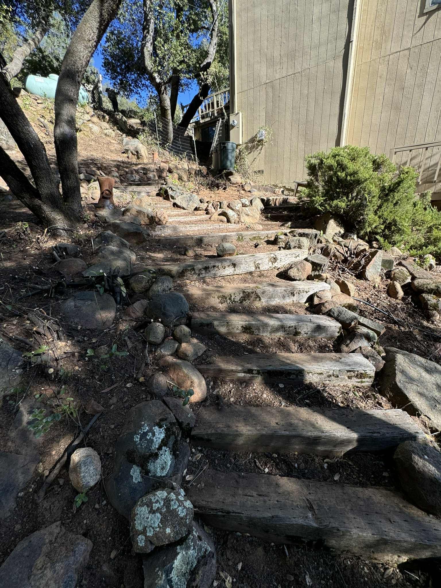 Stone steps lead uphill alongside a building and trees on a sunny day.