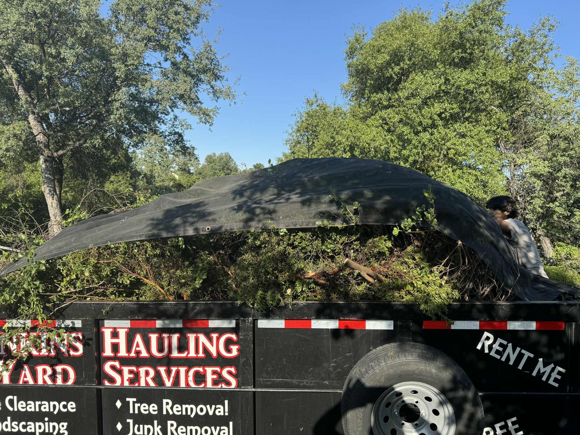 A trailer loaded with yard waste, covered by a tarp, with