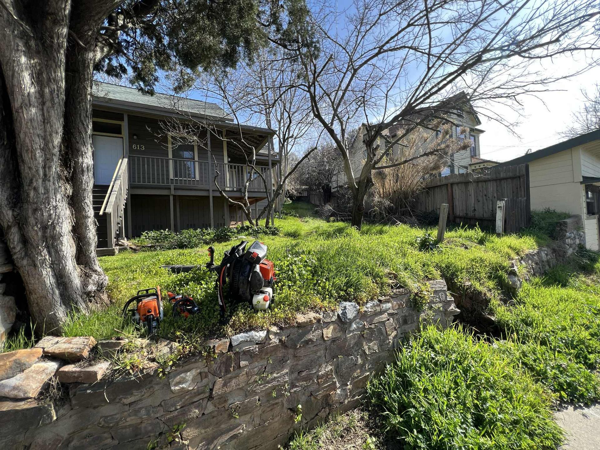 A grassy, sloped yard with a house and a chainsaw.