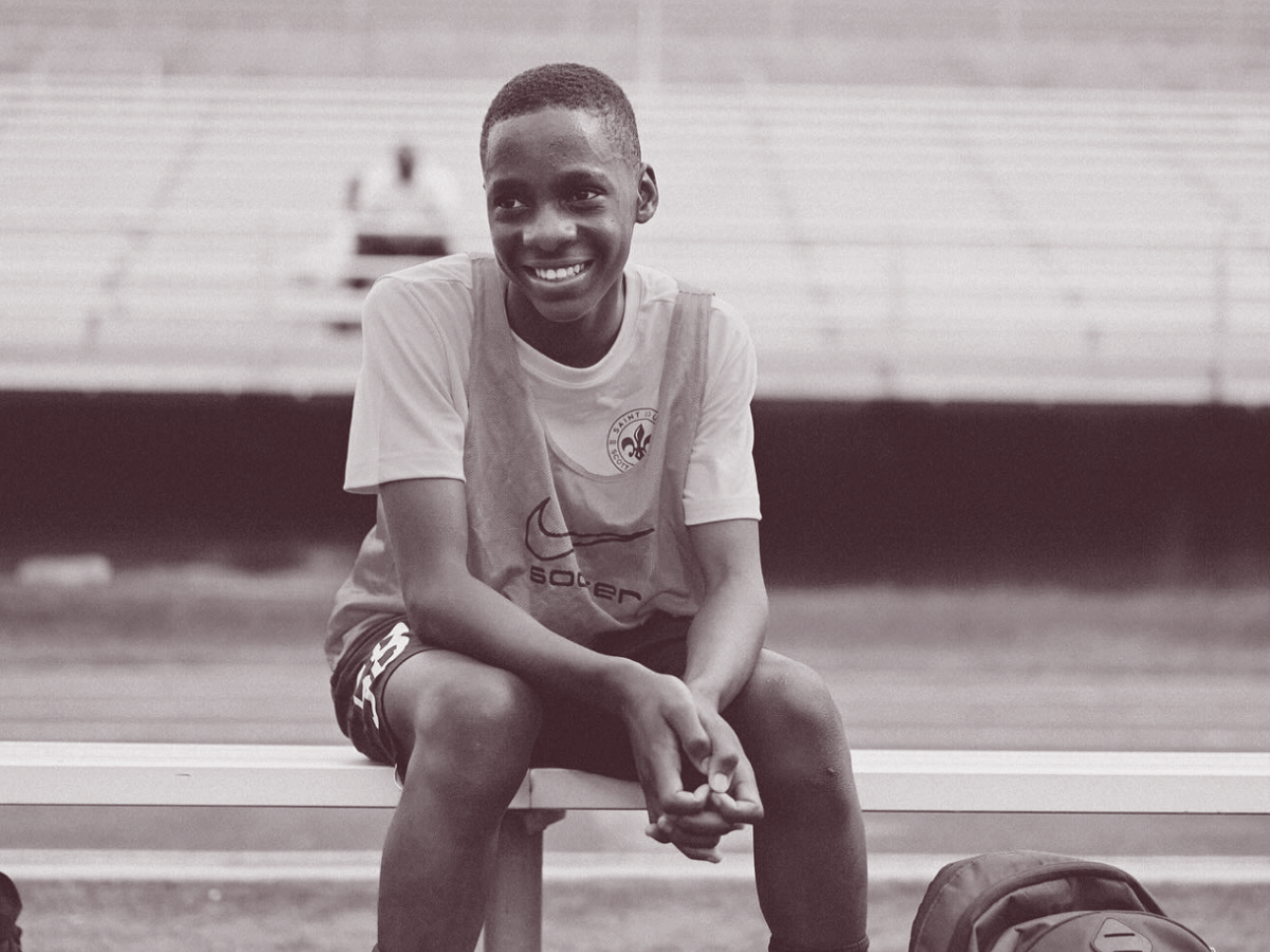 Smiling person sitting on a track bench in a stadium, wearing a light shirt and shorts.