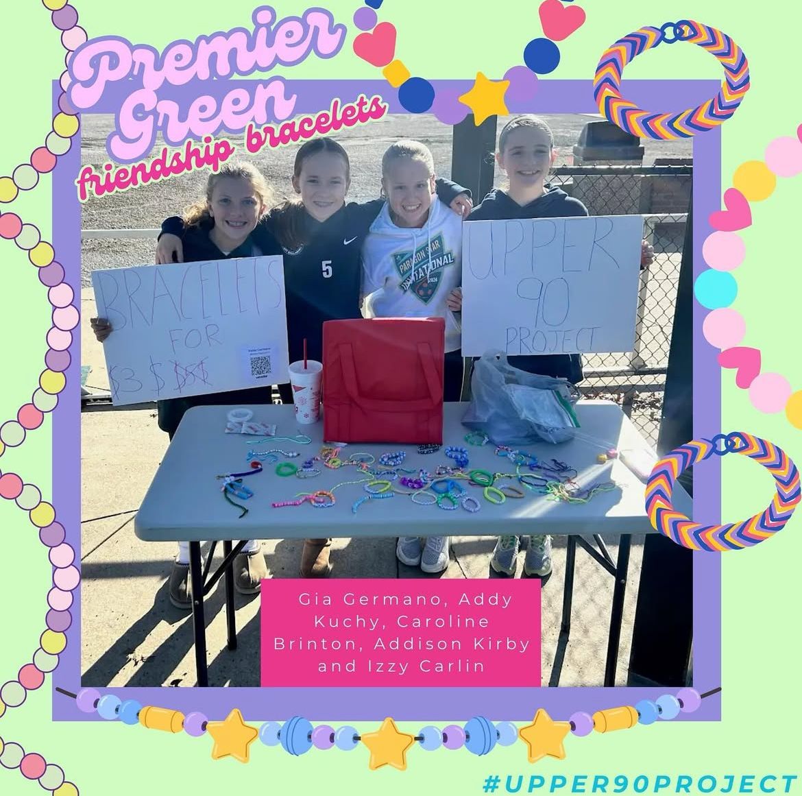 Three people at a decorated table with colorful Premier Green Friendship bracelets signs and a pink donation box.