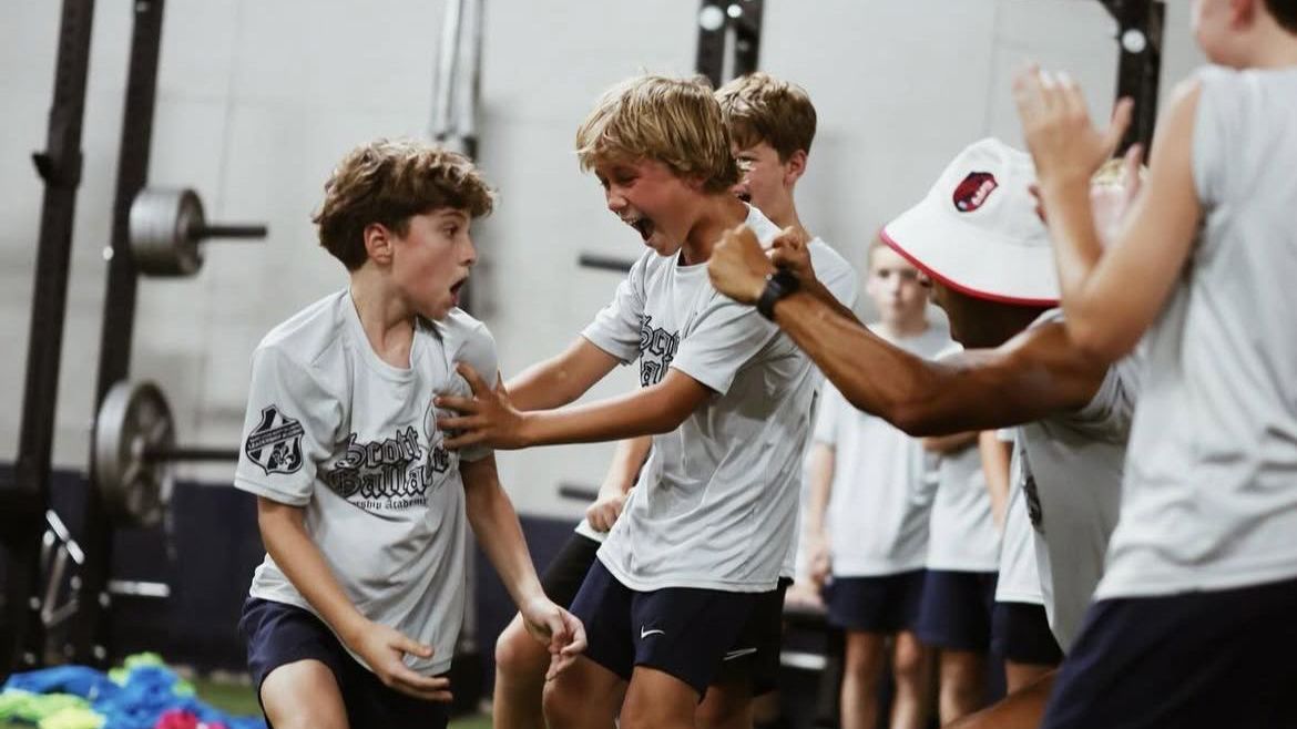 Youth athletes in white jerseys high-five on a gym floor during practice