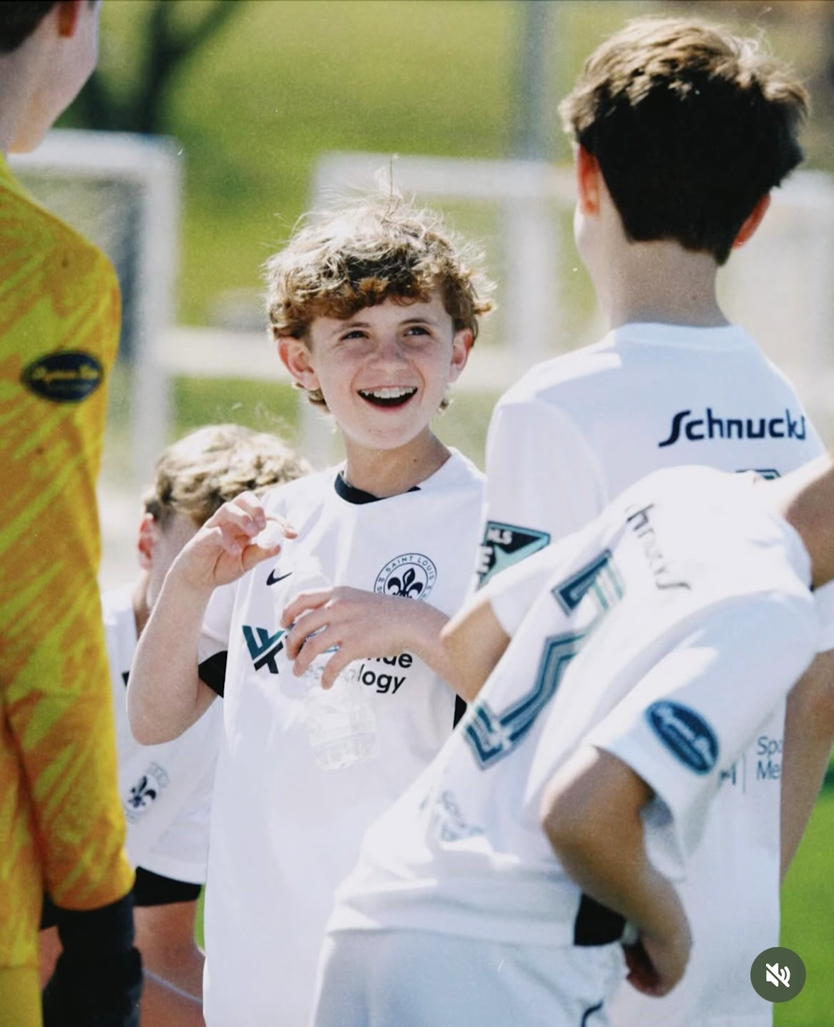 Smiling child in a white soccer jersey talking to teammates outdoors