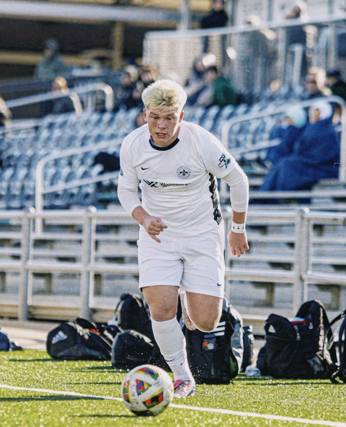 Soccer player in white dribbles a ball on the field near team benches