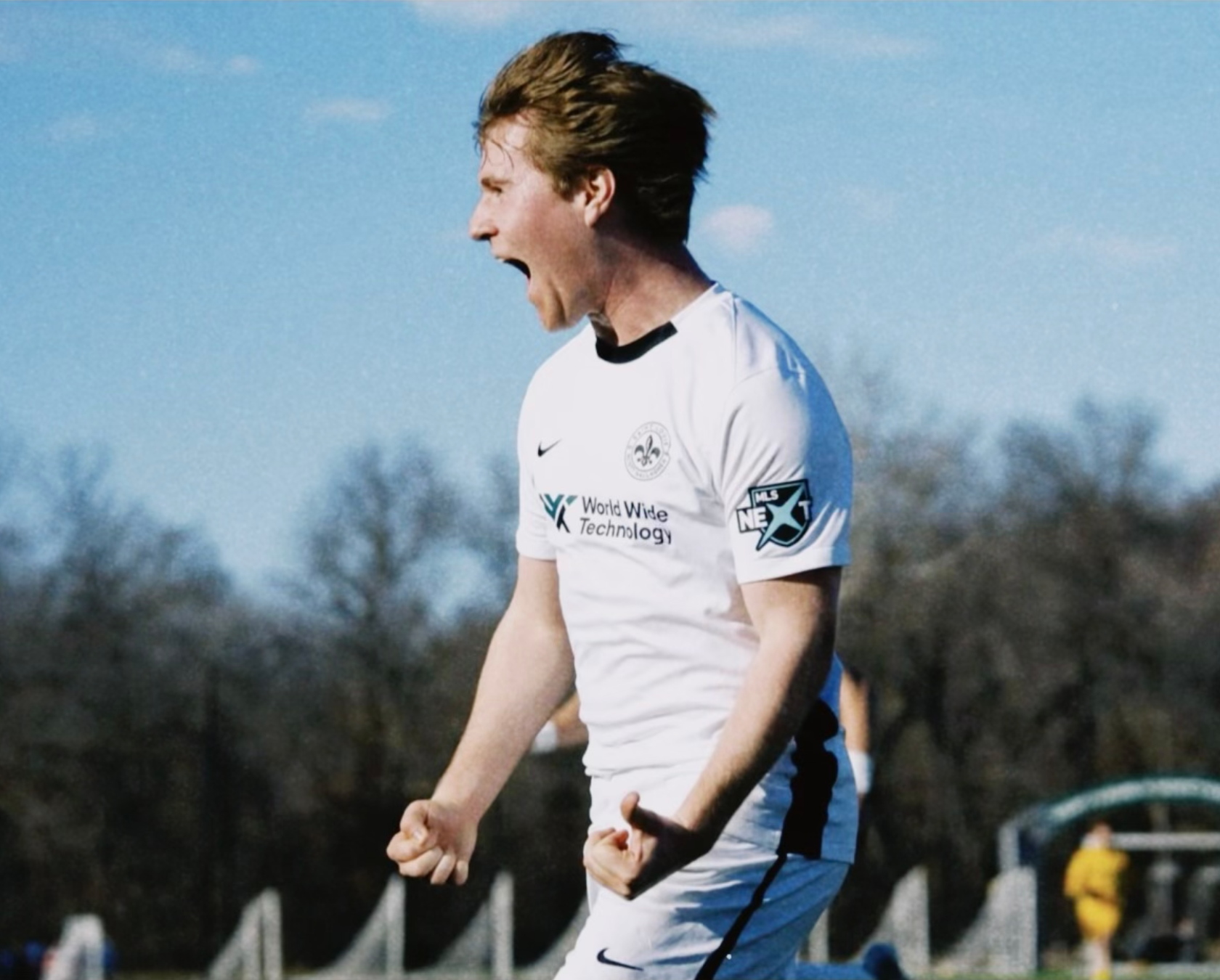 Soccer player in white jersey celebrating on the field, shouting with clenched fists