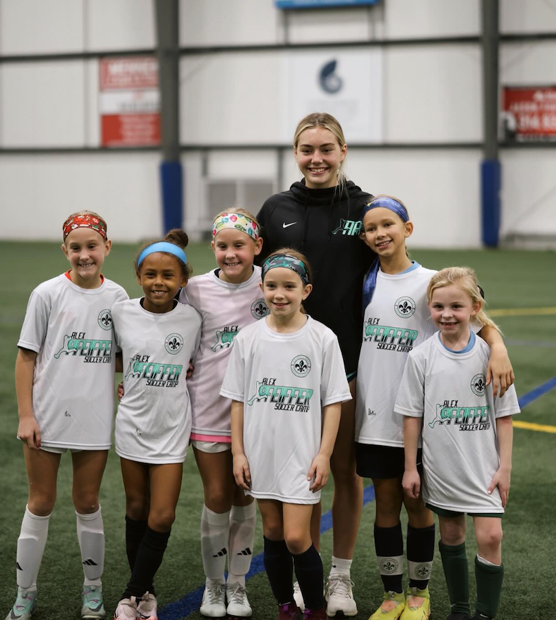 Youth soccer team posing indoors with coach in white uniforms, smiling for a group photo.